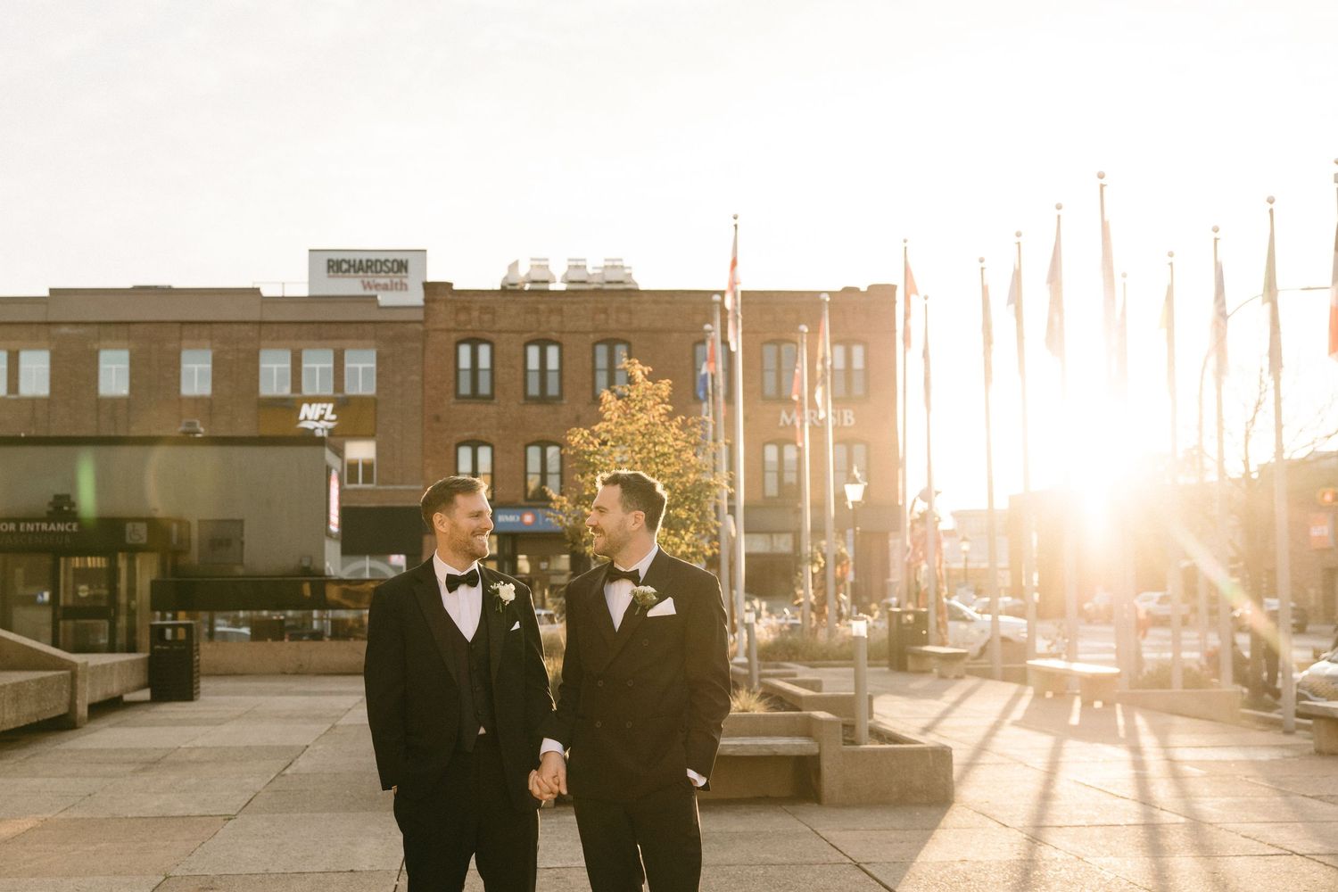 Two people in formal wear walking together at sunset in an urban setting.