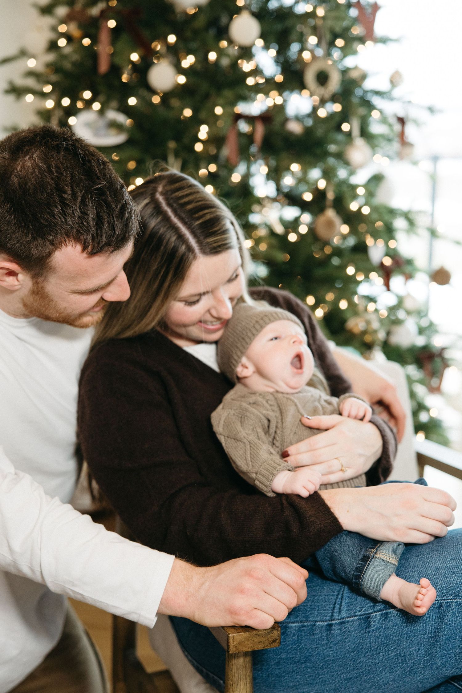 Parents sharing intimate moments with their baby by a festive Christmas tree.