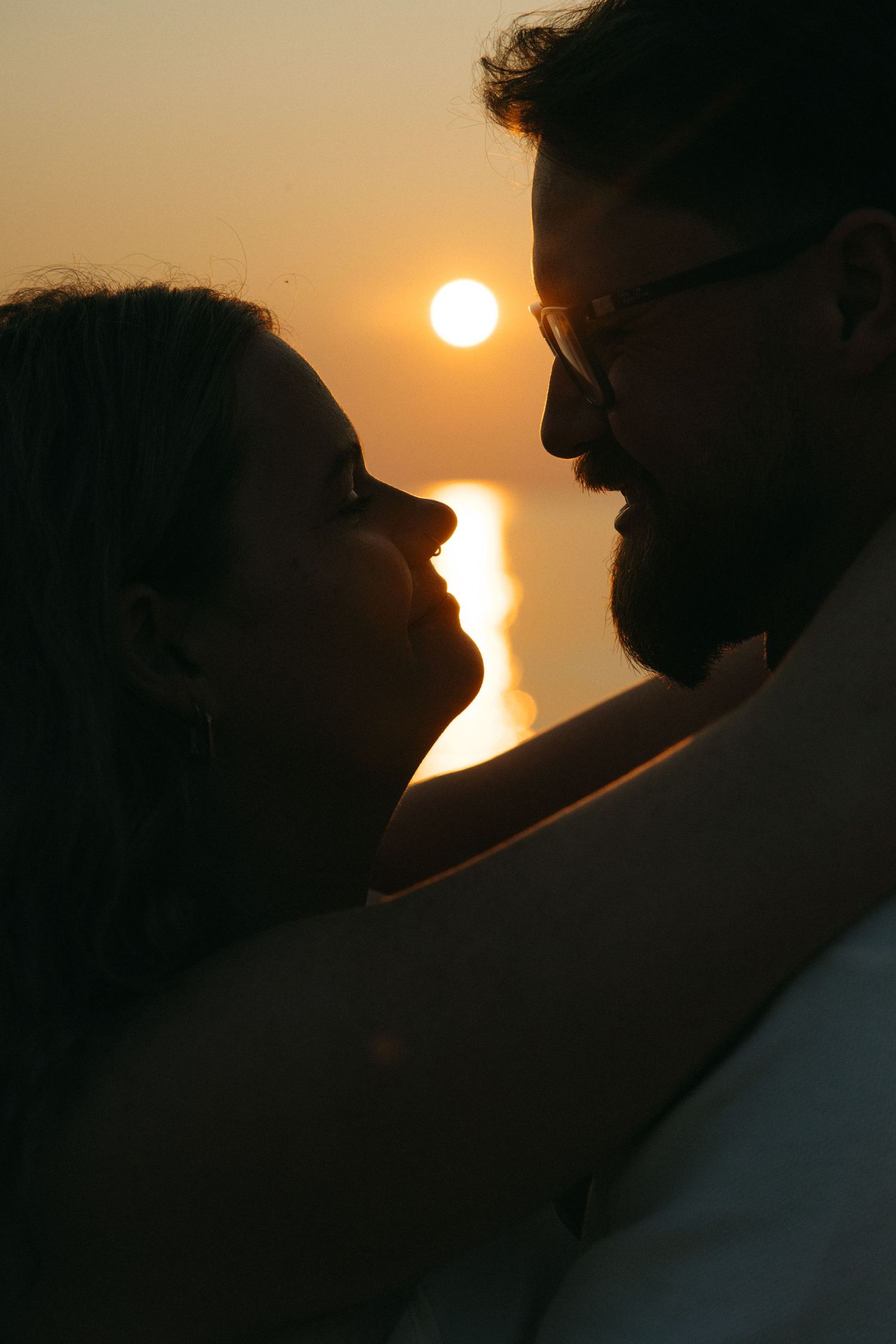 Romantic silhouette of couple nearly kissing with glowing sunset and ocean in background.
