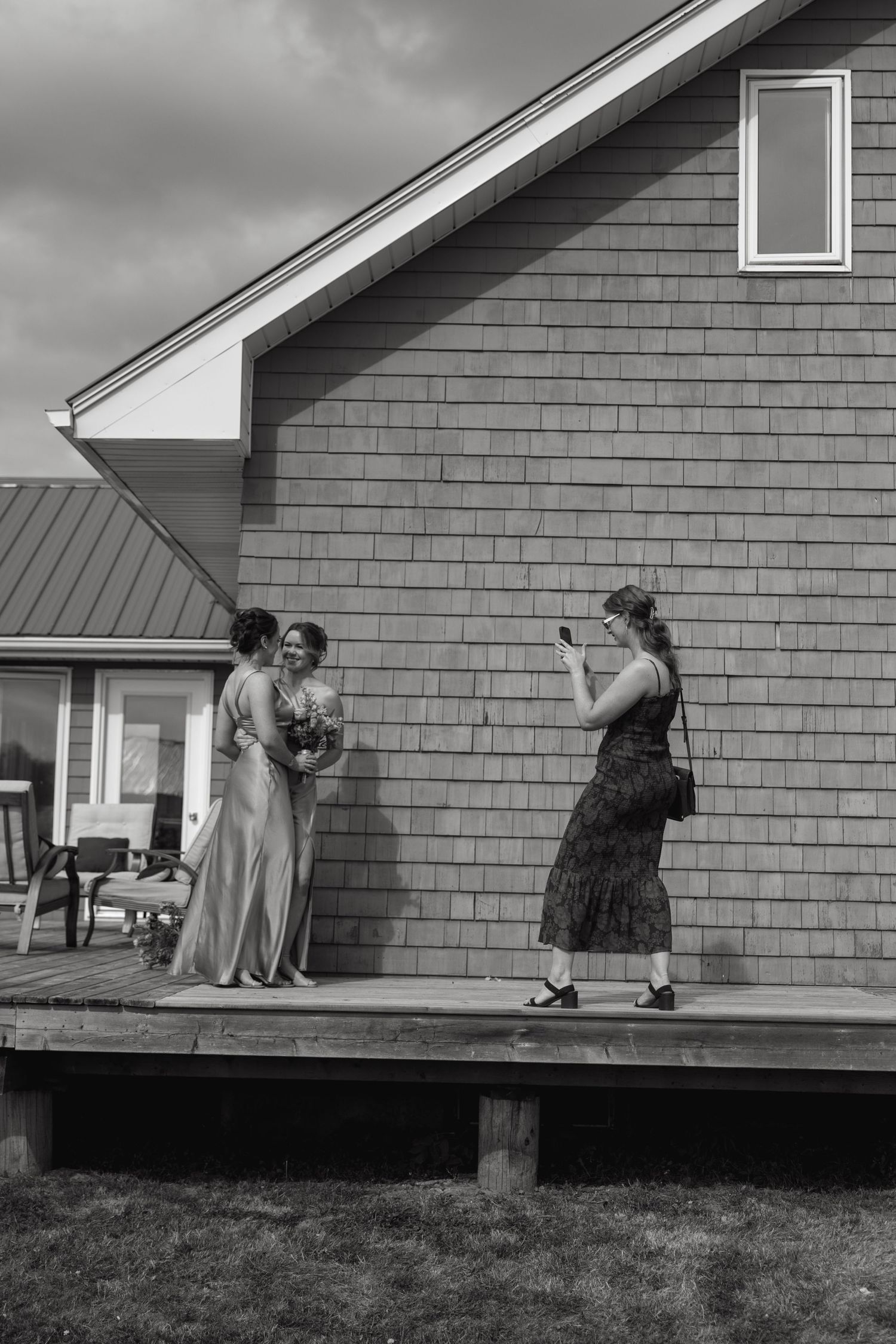 People in formal attire gathered on a deck outside a gray shingled house.