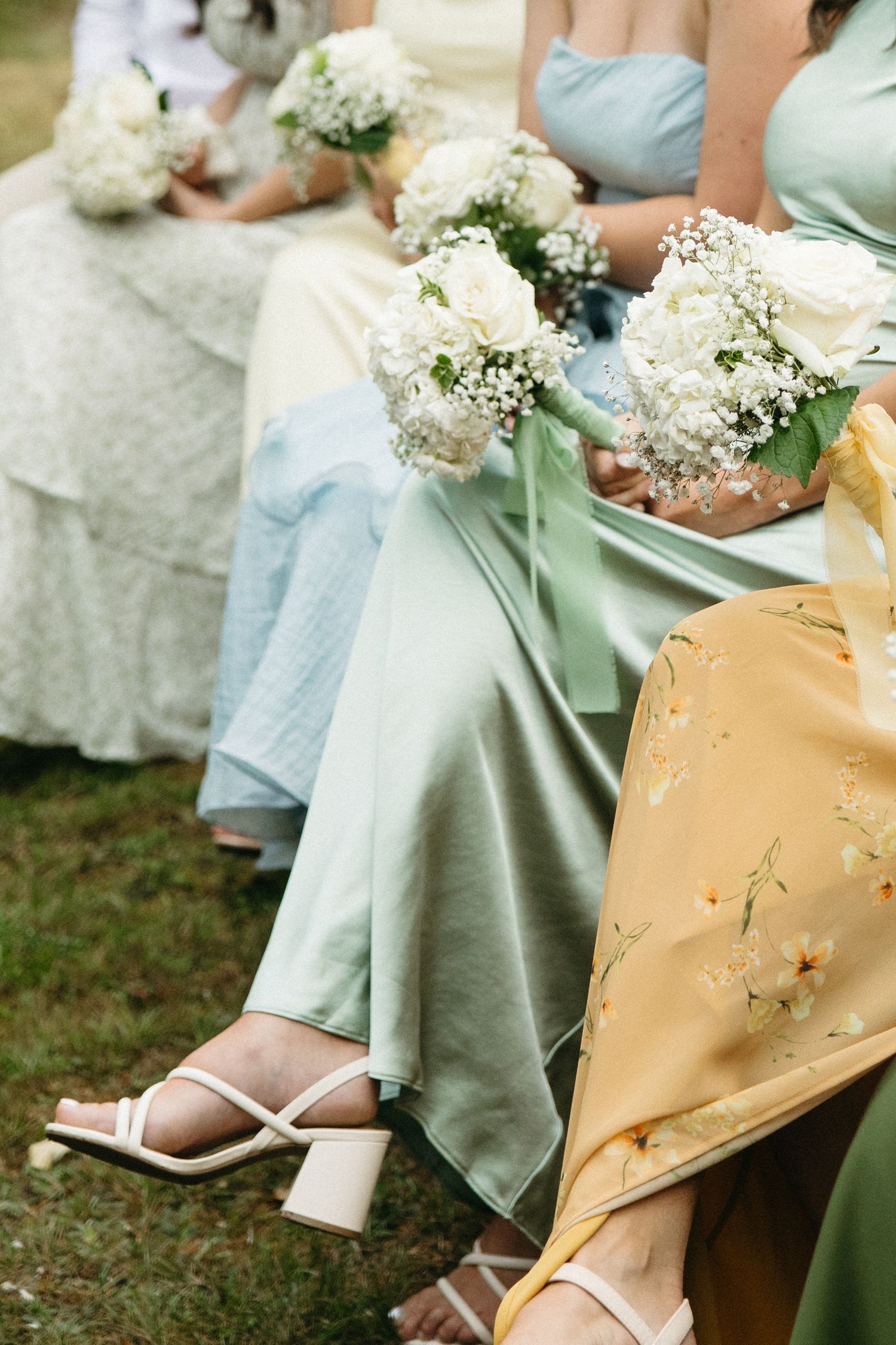 Close-up of bridesmaids' dresses in mint green and light blue with white floral bouquets.