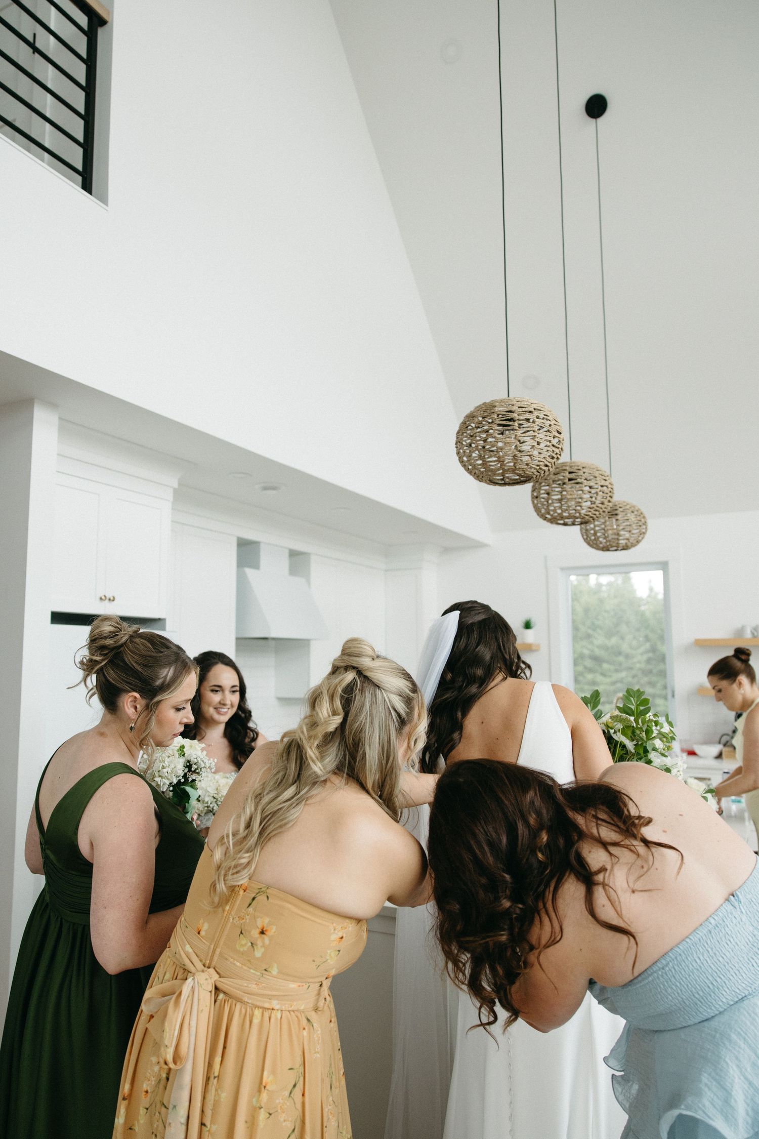 Wedding party members look out large windows in a modern white interior space.