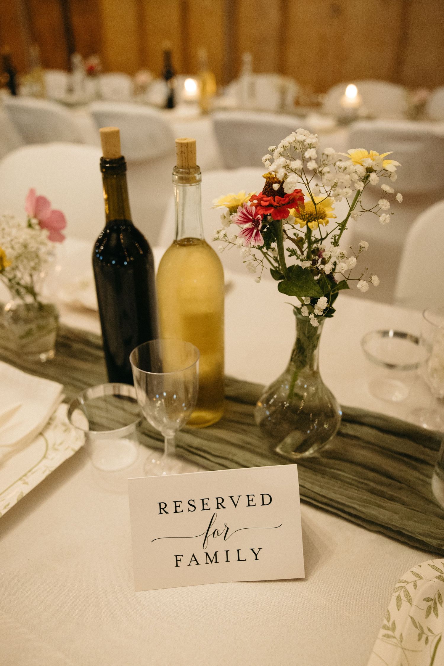 Wedding reception table settings with reserved and family signs, wine bottles, and delicate floral centerpieces.