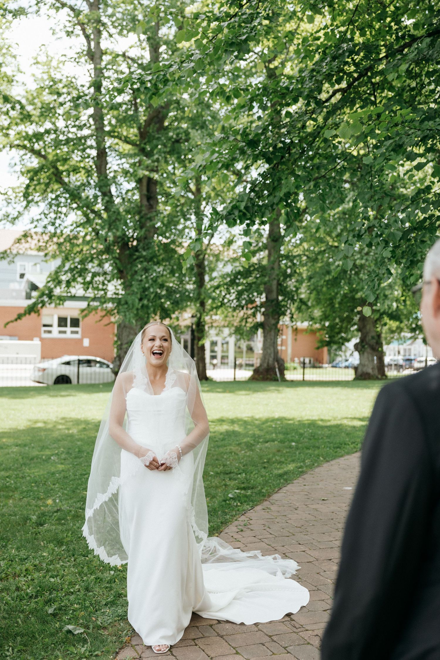 Bride in white dress walking along a tree-lined path during wedding day.
