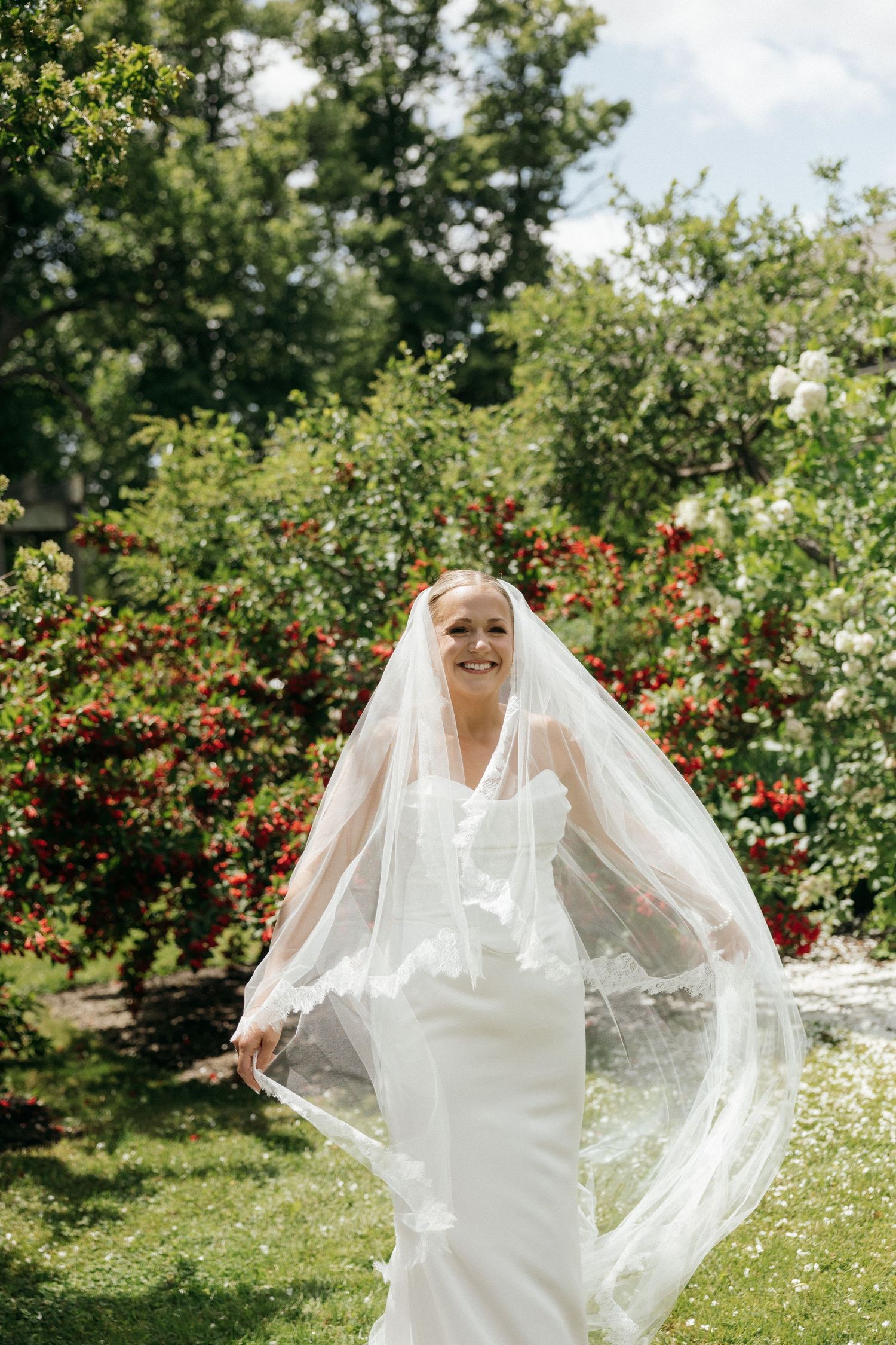 Elegant bridal portrait in a garden with flowing veil and white dress among blooming flowers.