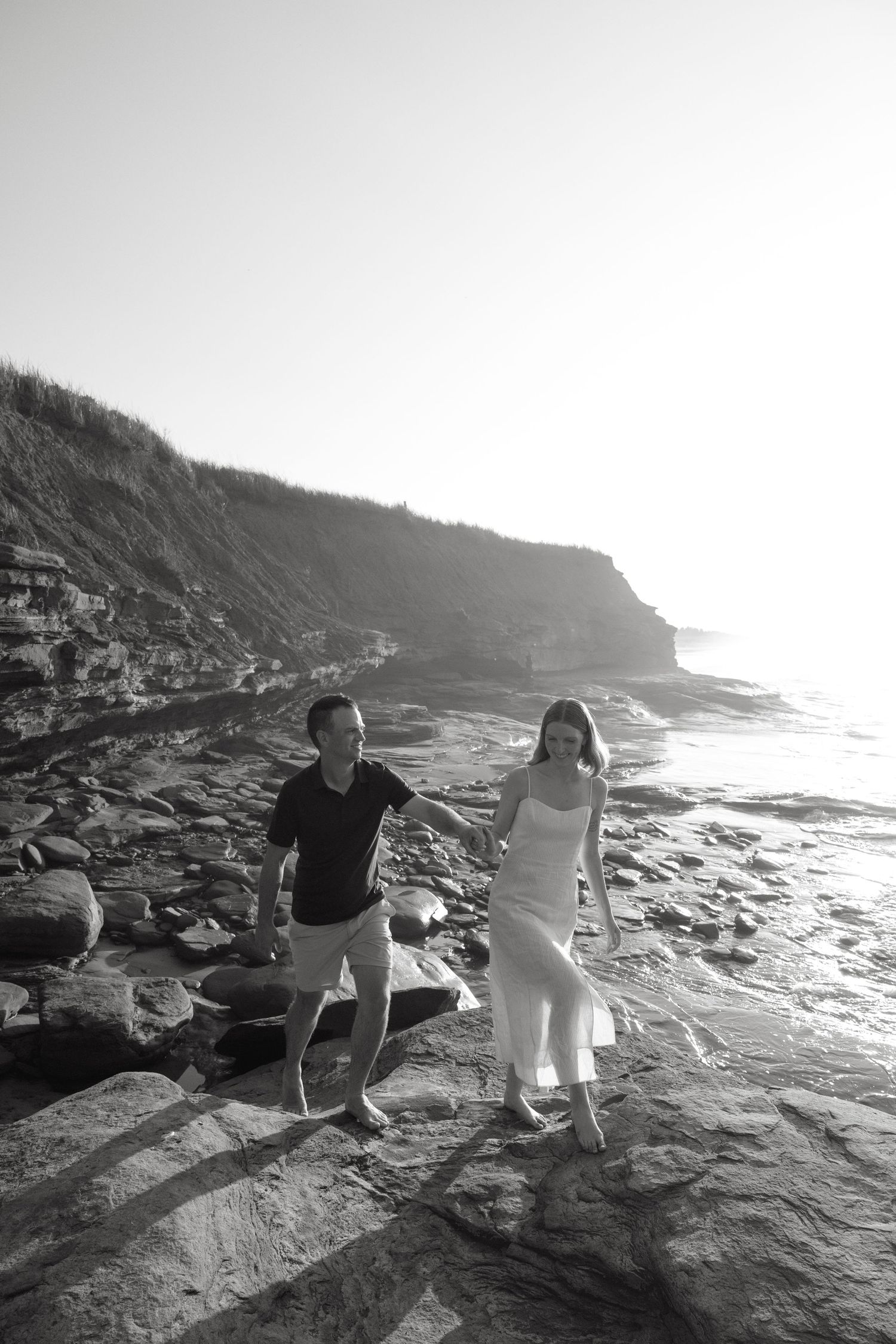 Black and white photo of two people walking along rocky coastal cliffs.