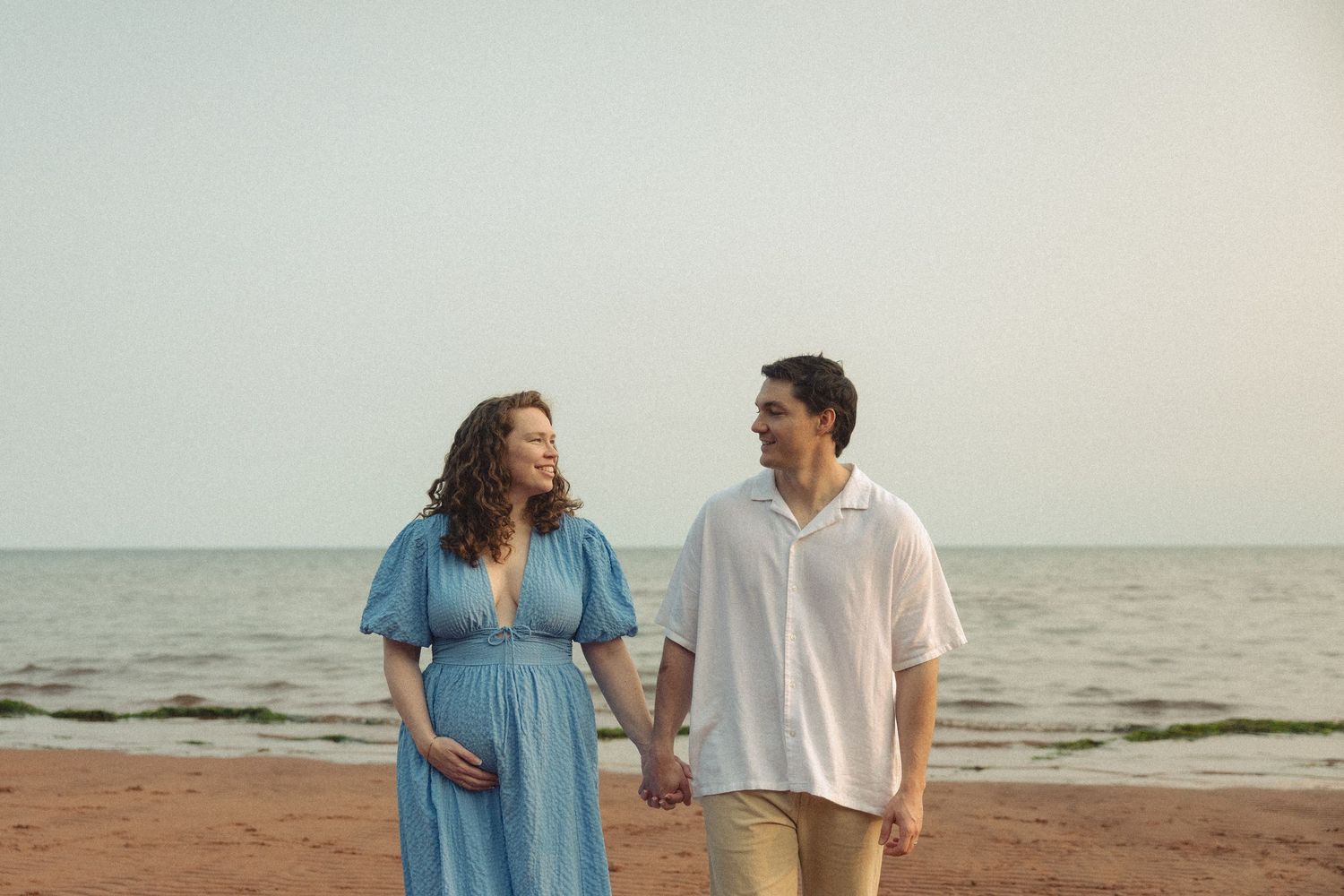 A couple shares tender moments while walking along the shoreline at sunset.