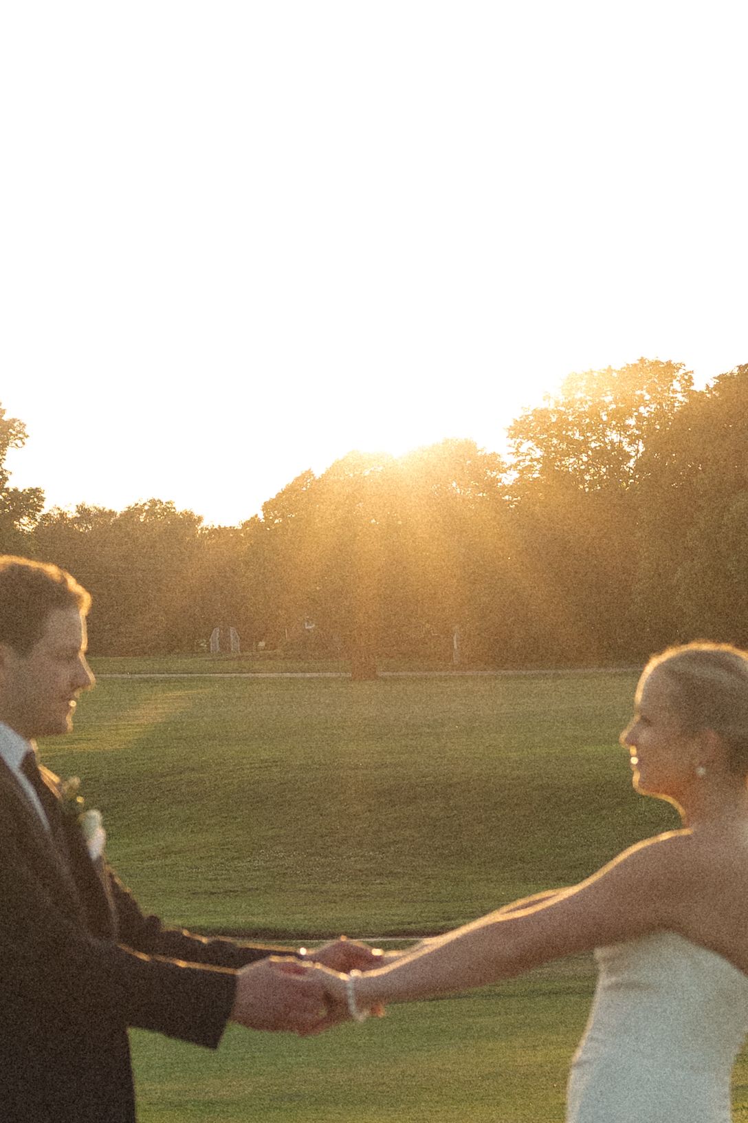 A couple holding hands during golden hour sunset in an outdoor field.