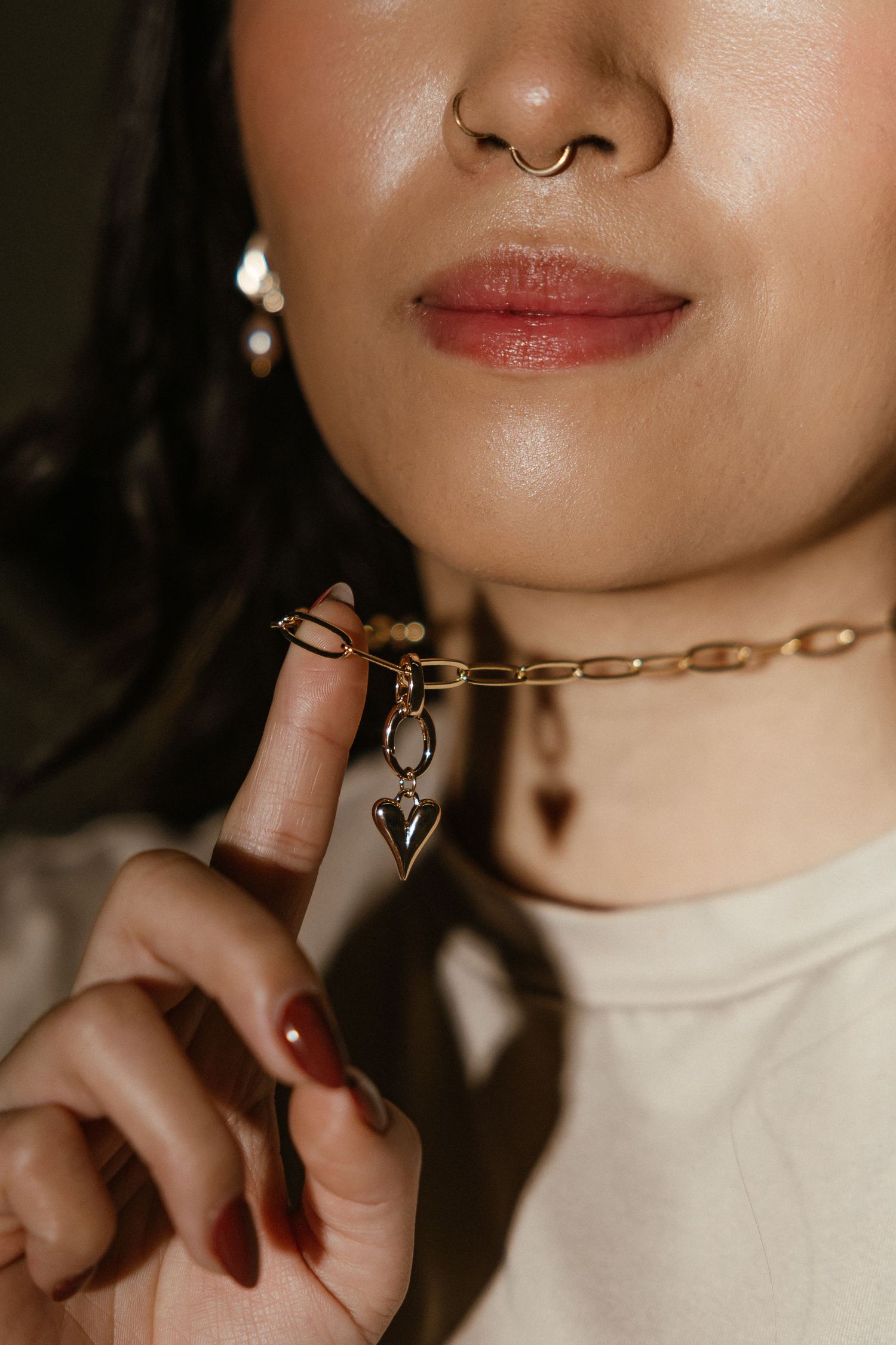 Close-up view of jewelry and makeup details showing glossy lips, pearl earrings and a delicate gold chain necklace.