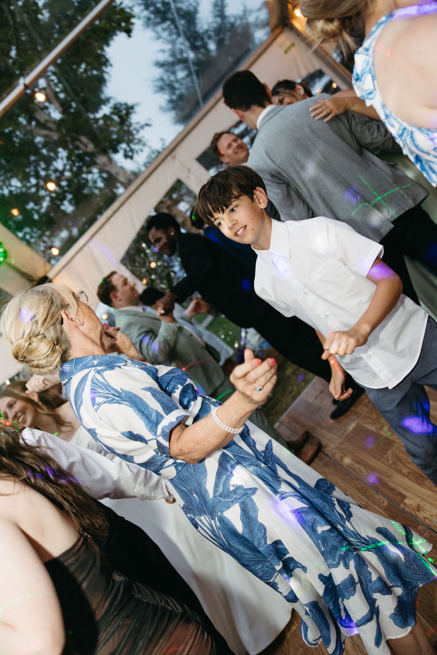 Young boy dancing with older woman in blue floral dress at wedding reception.
