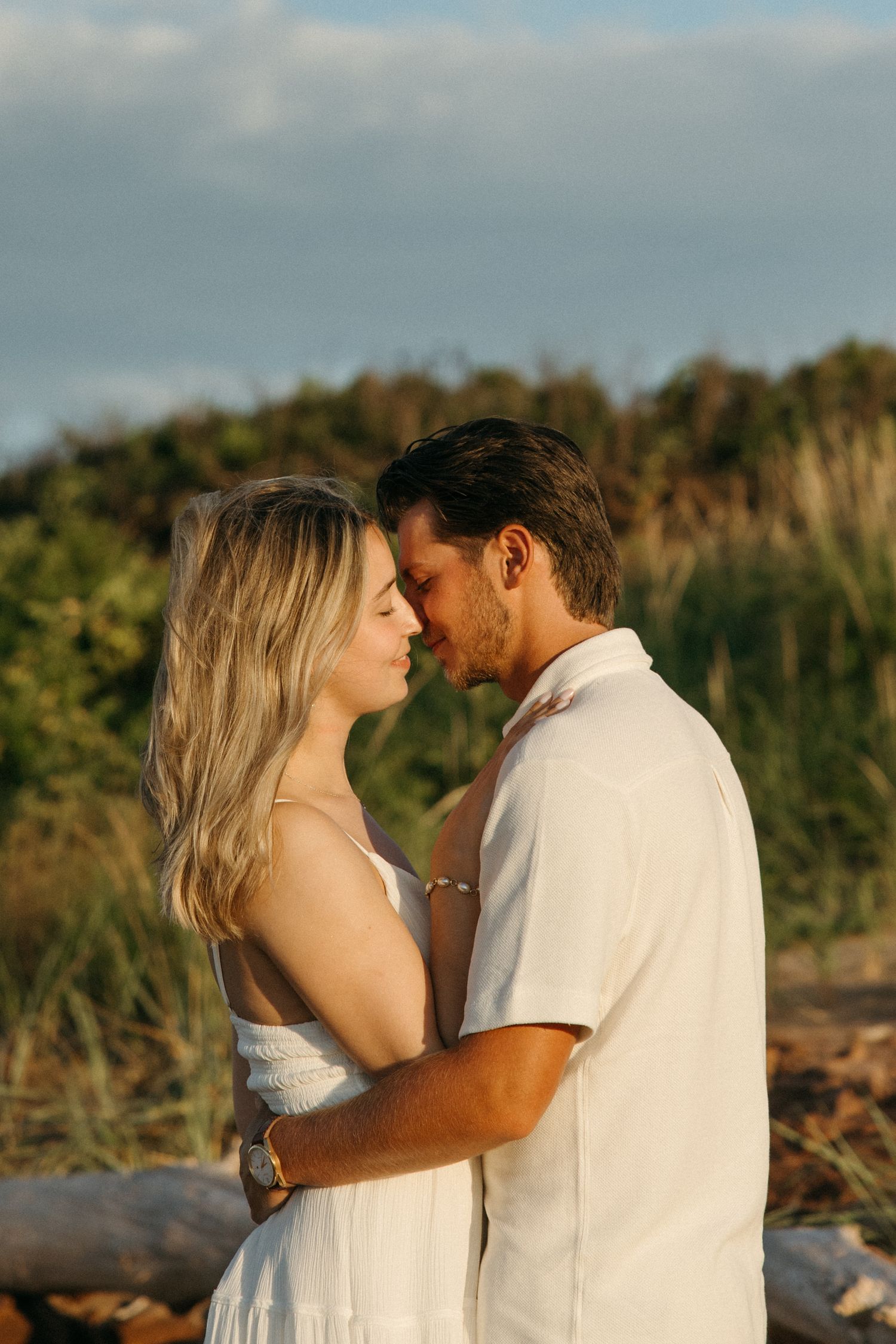 A couple sharing a tender moment outdoors at golden hour near lush greenery.