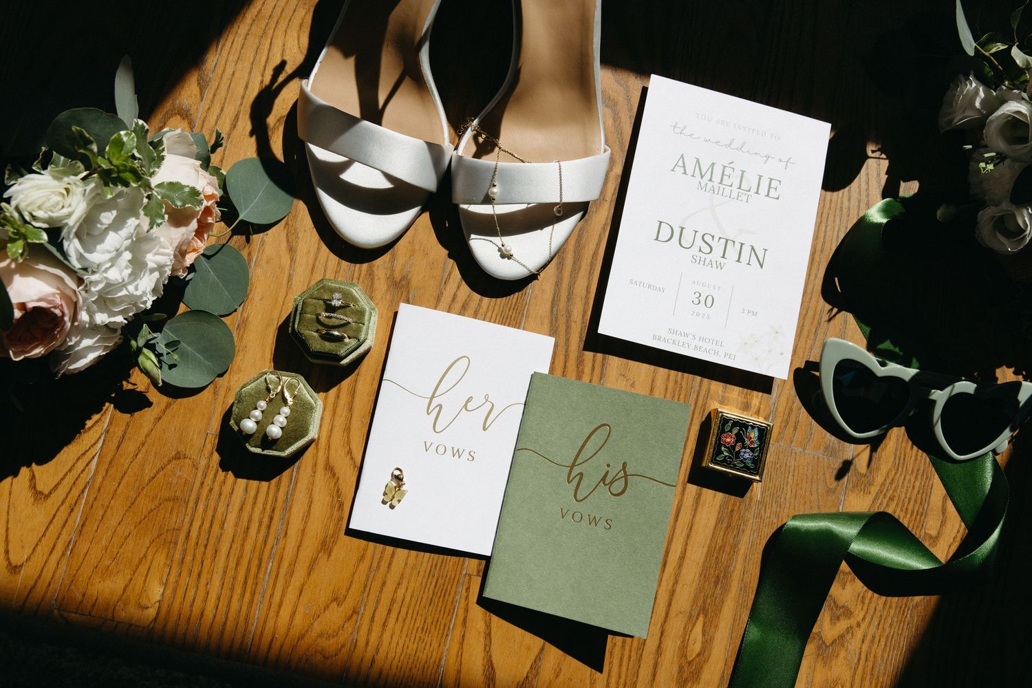 Elegant wedding flat lay featuring invitation suite, bridal heels, bouquet, vow books, and green ribbon.