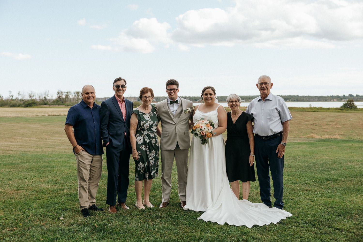 Wedding party family portrait on a green lawn with a waterfront view on a sunny day.