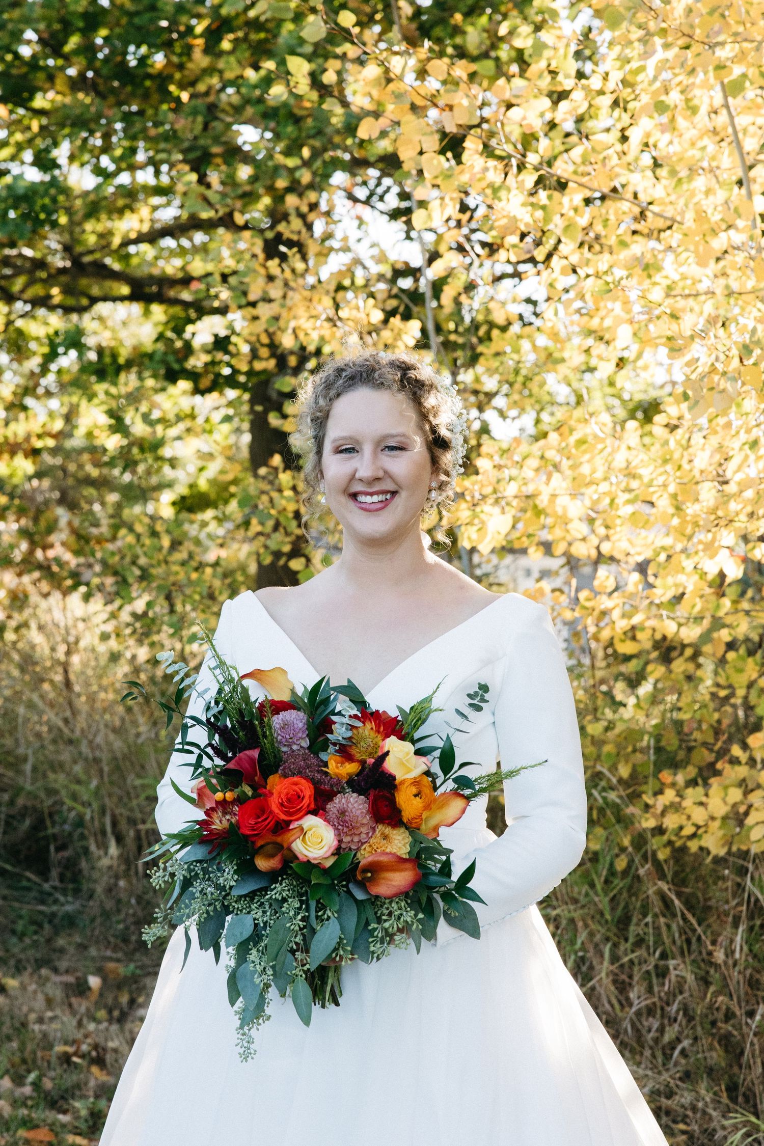 Autumn wedding portrait with vibrant fall foliage and colorful bouquet.