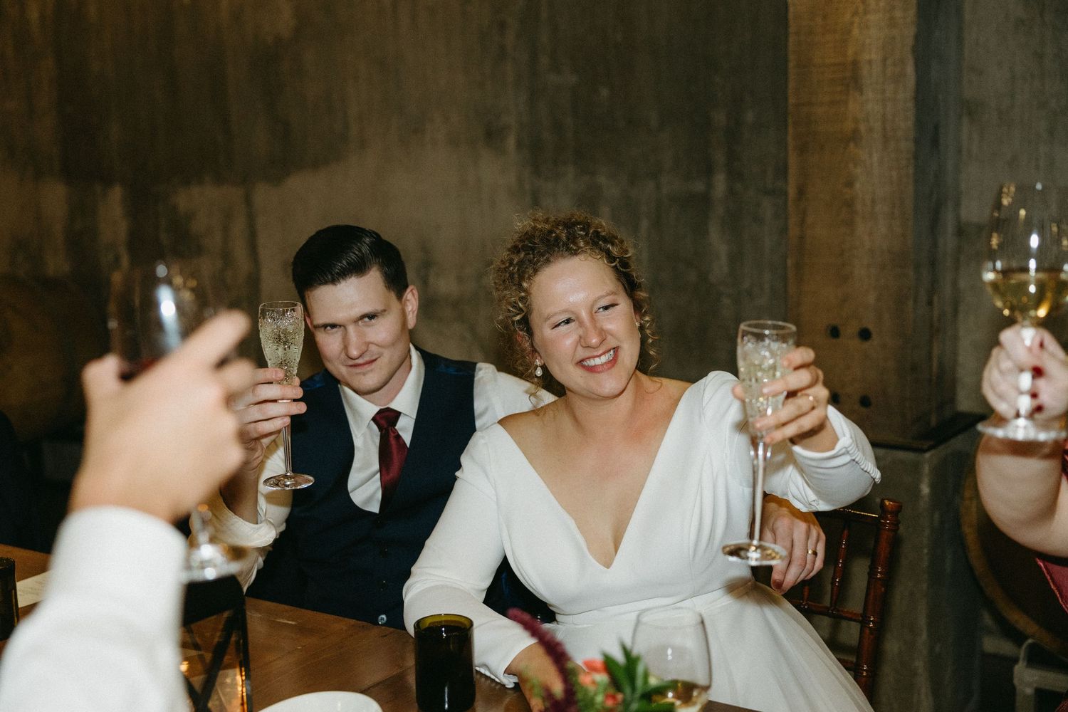 Wedding reception guests toasting with drinks in a dimly lit venue.
