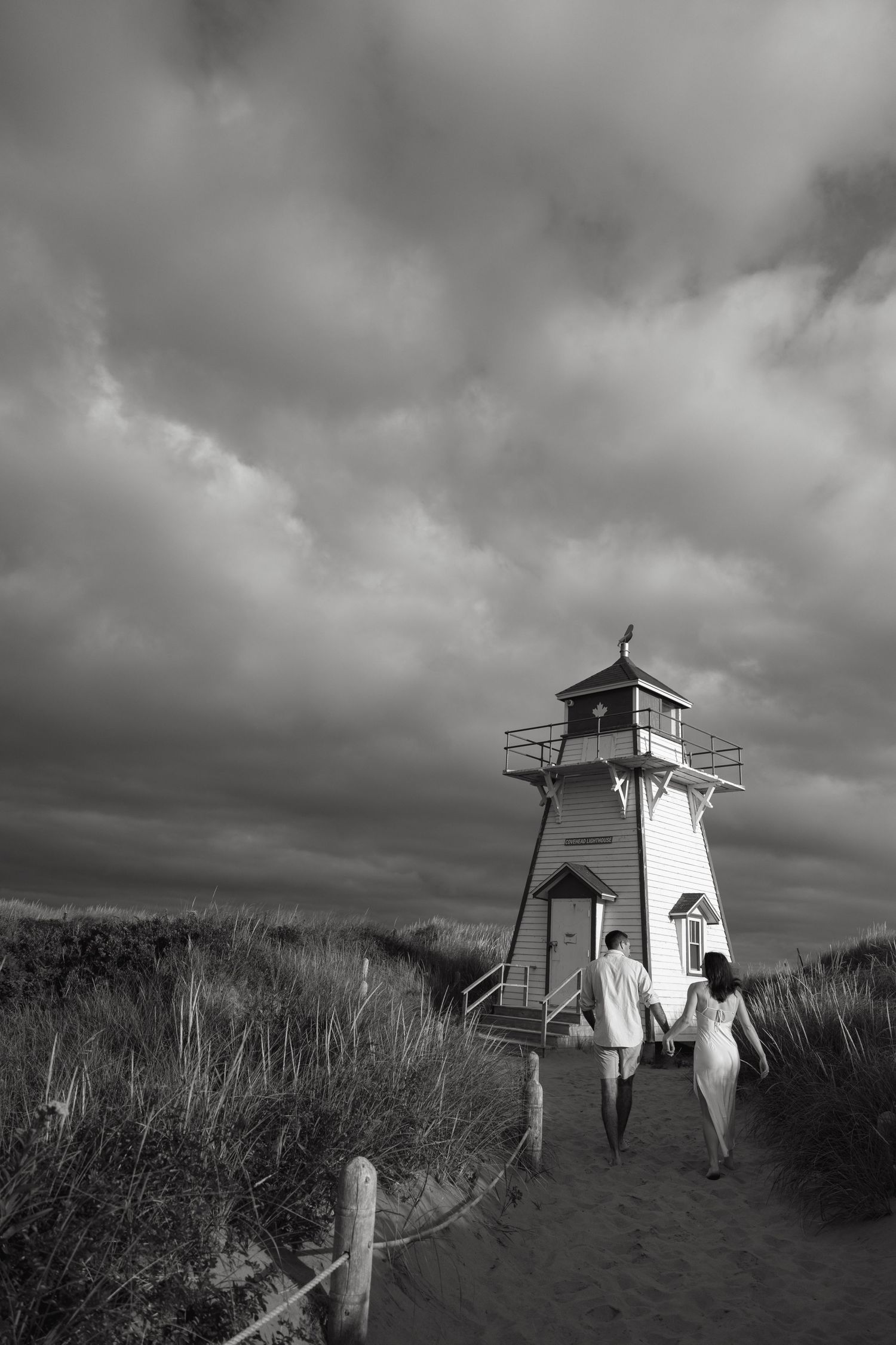 Black and white photos of lighthouse on sandy beach with dramatic stormy sky.