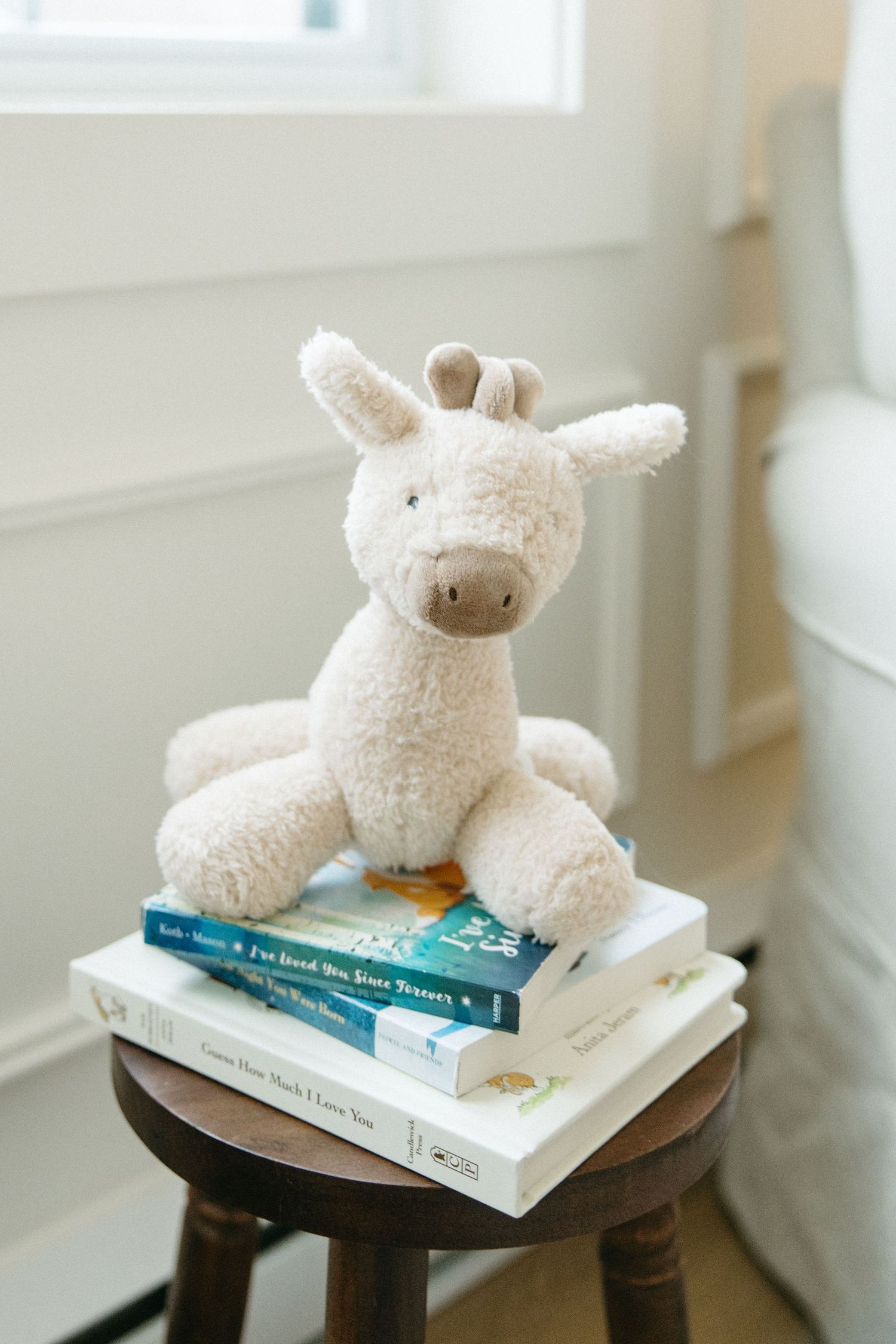 White plush stuffed animals arranged on stack of children's books on wooden side table.