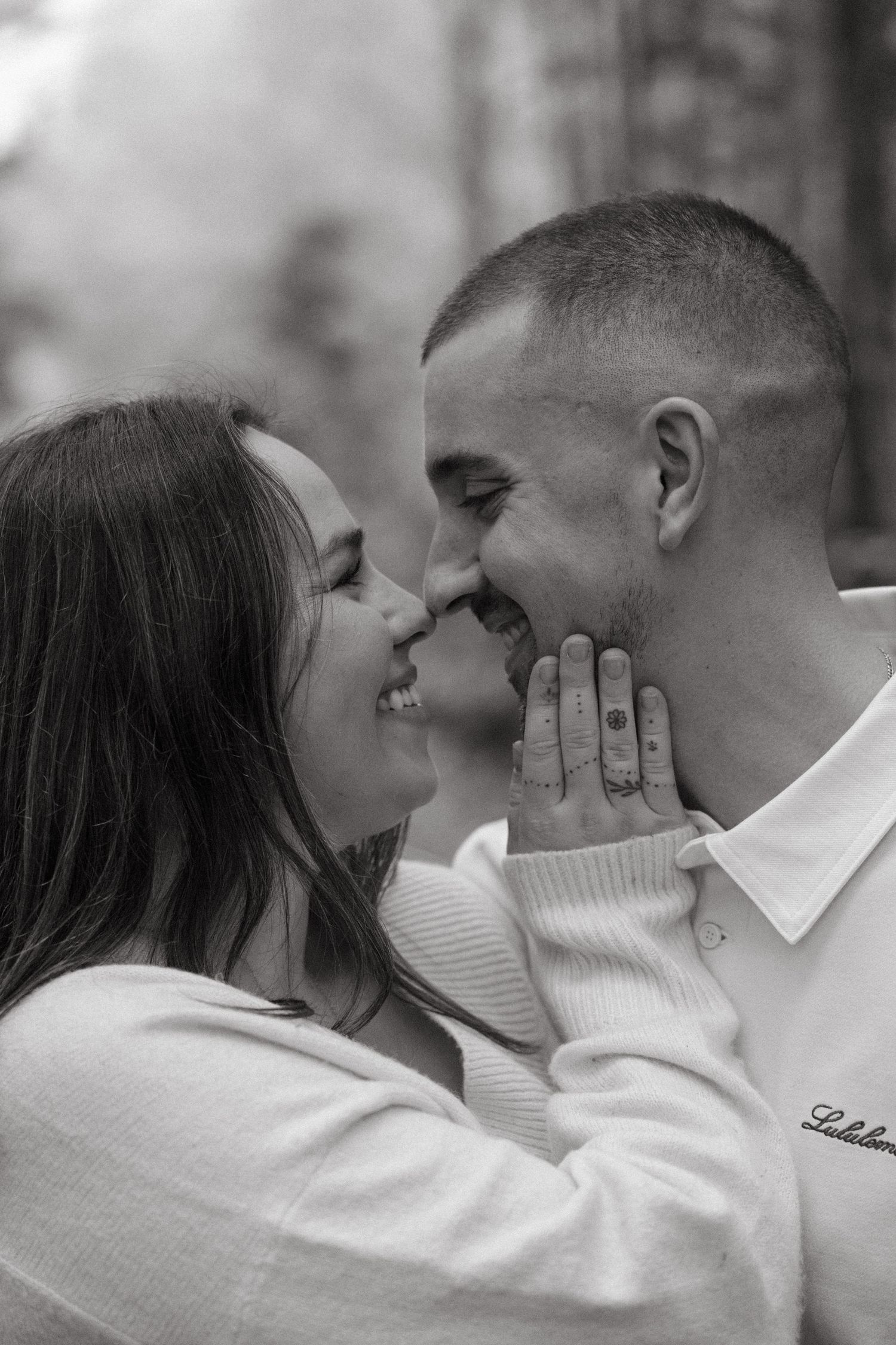 Two people in cream sweaters share an intimate moment against a backdrop of autumn trees.