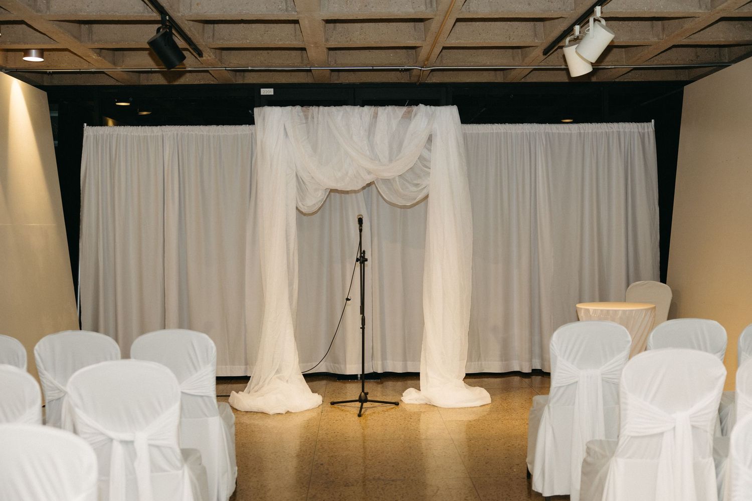 White draped ceremony arch with chairs set up for indoor wedding ceremony.