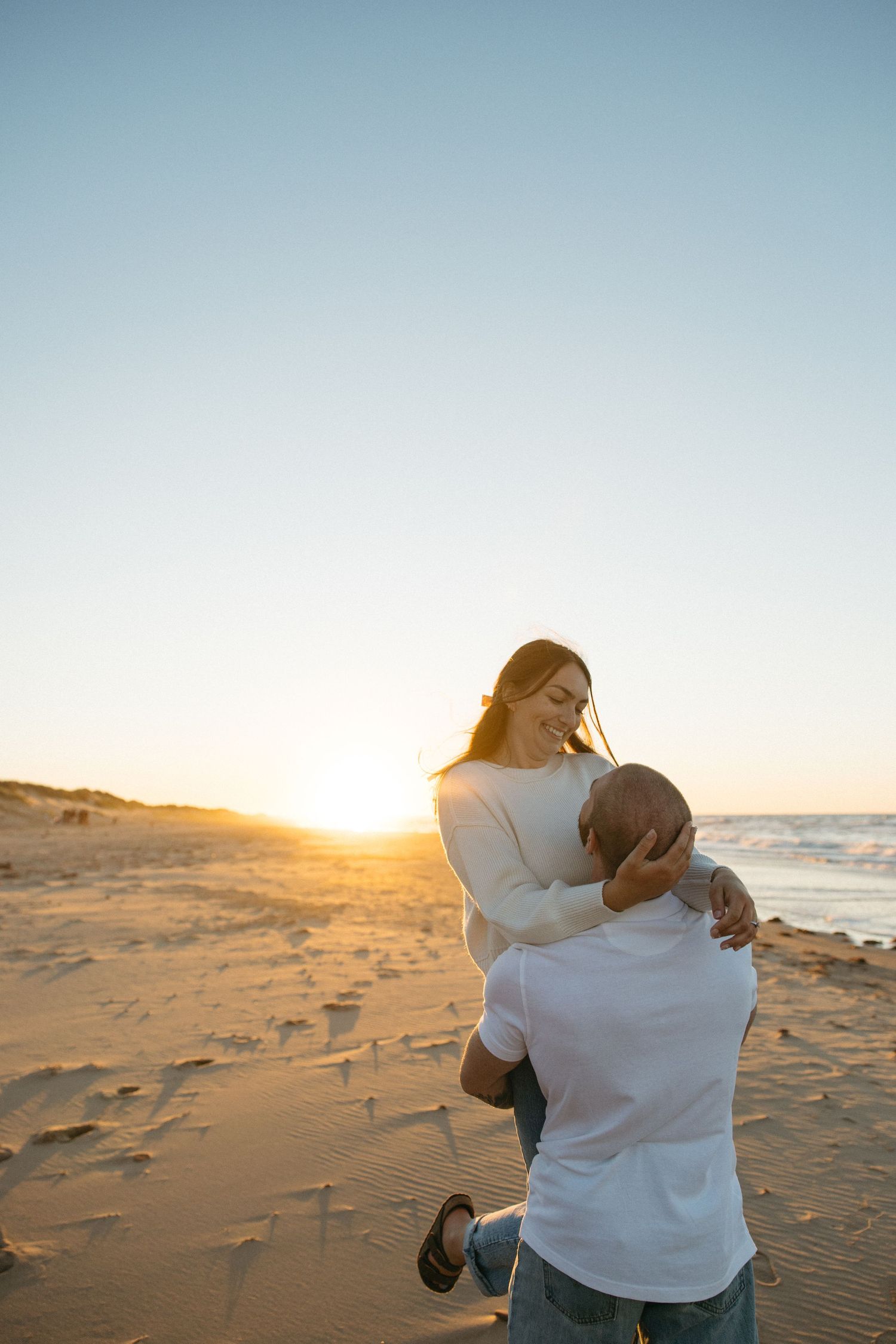 Couple embraces on beach at golden hour with ocean waves in background.