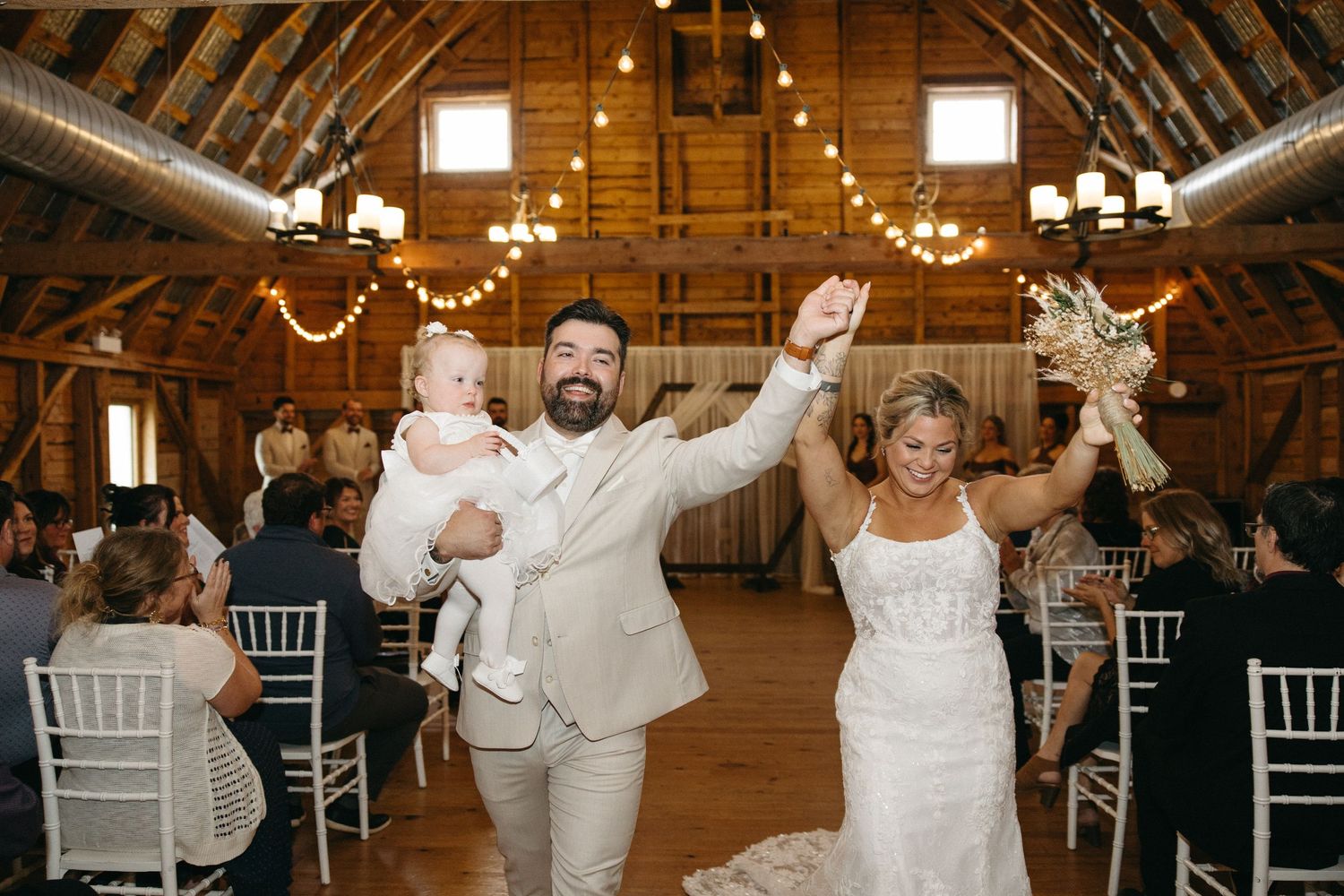 Wedding celebration in rustic barn venue with string lights and white chairs.