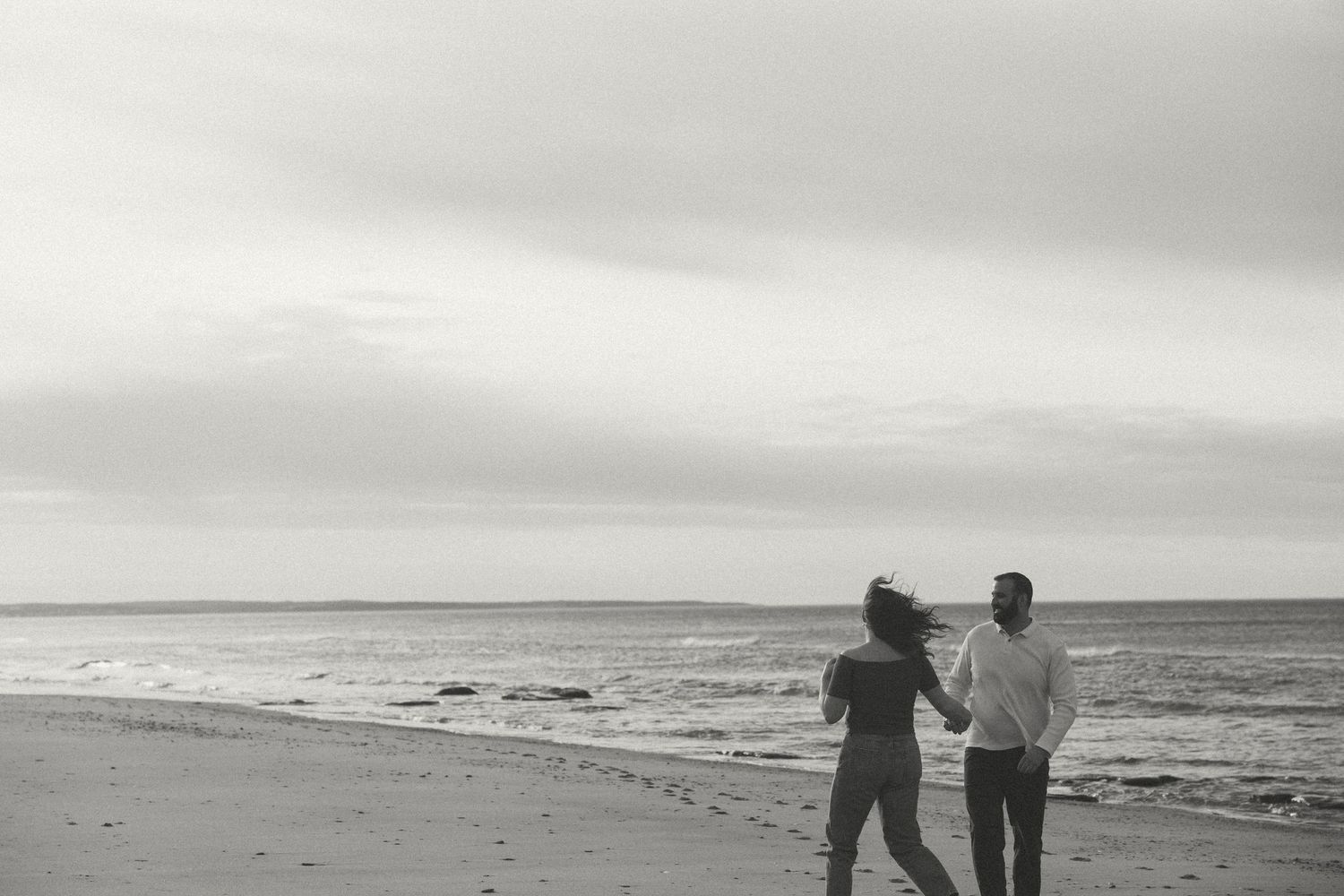 Couple walking hand in hand along a misty beach at sunset.