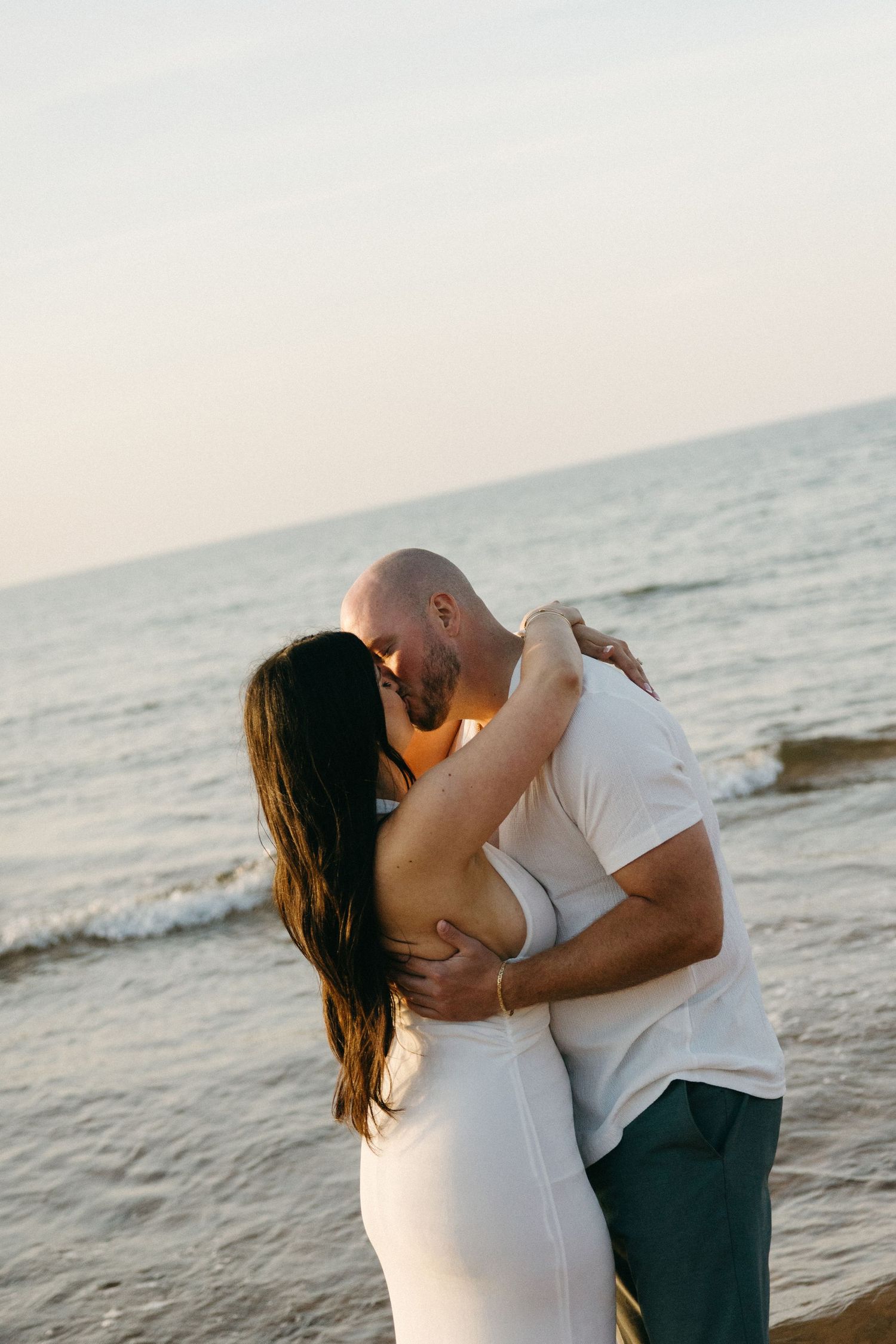 A romantic couple embracing and kissing on a beach at golden hour with ocean waves in the background.