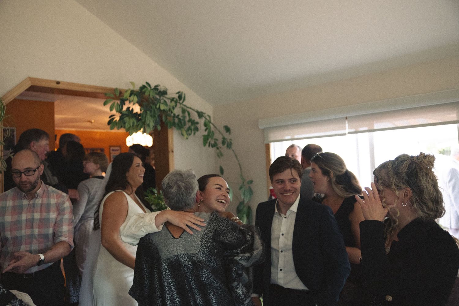 Wedding guests gather indoors sharing laughter and conversation during a reception celebration.
