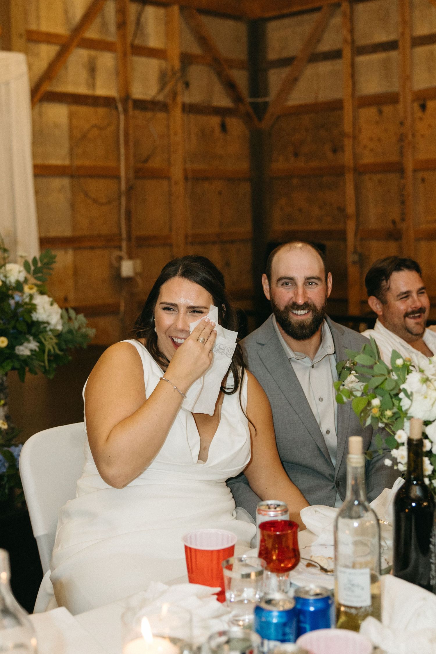 A couple shares a joyful moment at their wedding reception table with elegant floral centerpieces.
