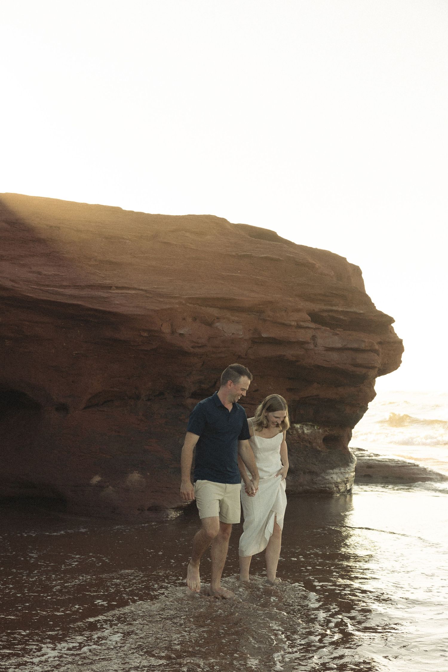 A couple enjoys a moment together by red coastal cliffs as waves roll in at sunset.