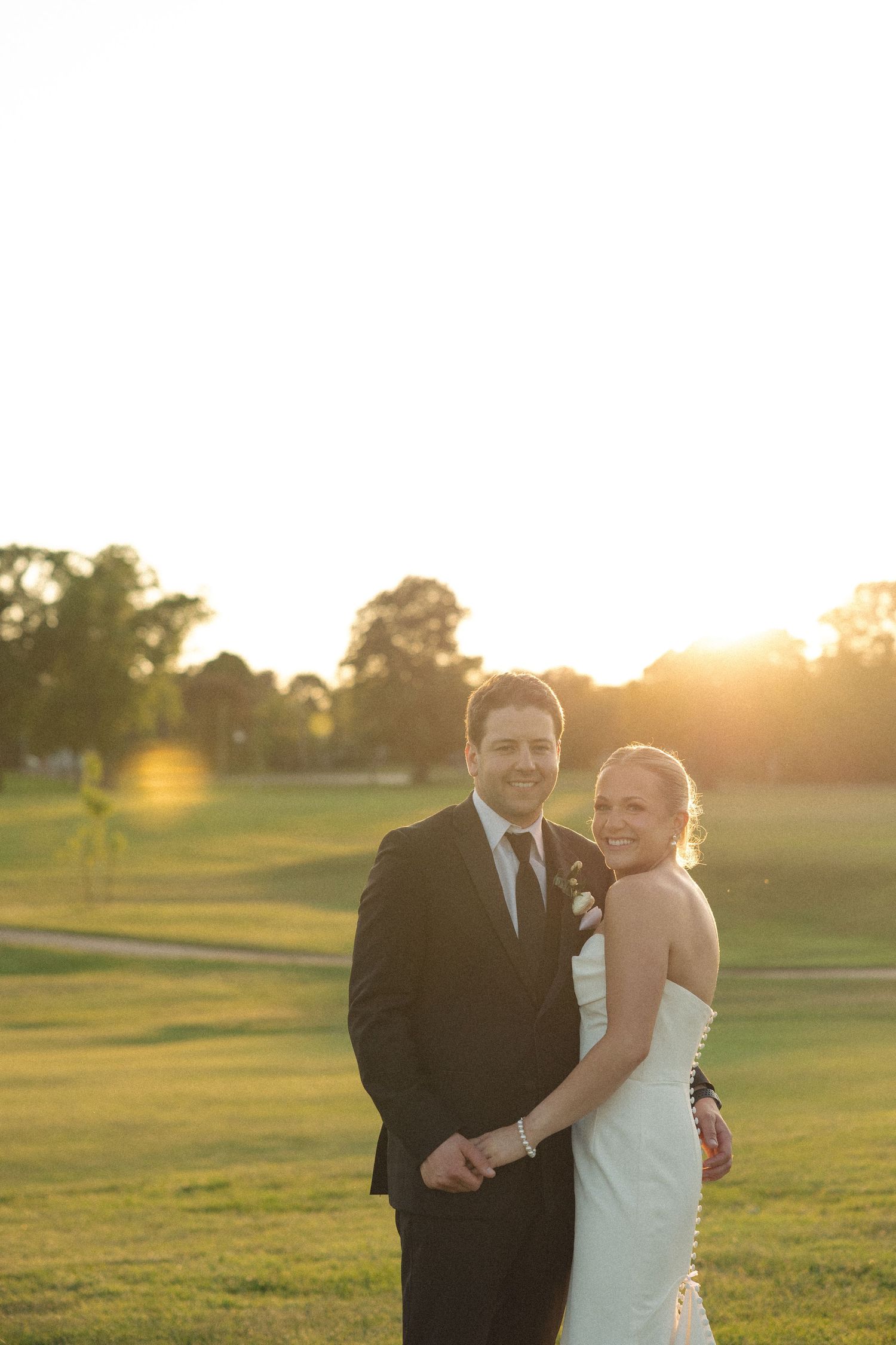 Newlyweds pose together during golden hour on a golf course.