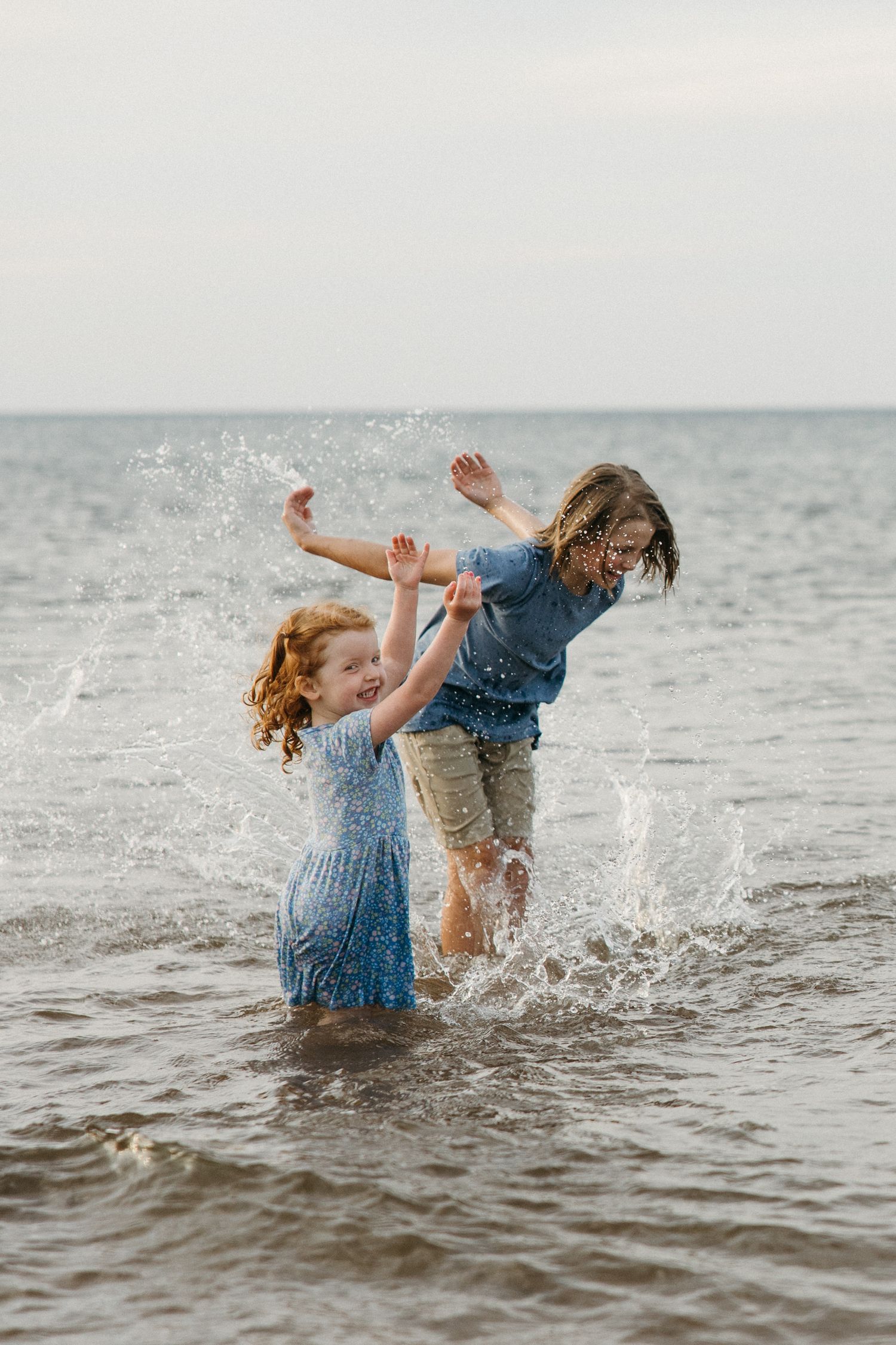 Two children splashing and playing joyfully in ocean waves at the beach.