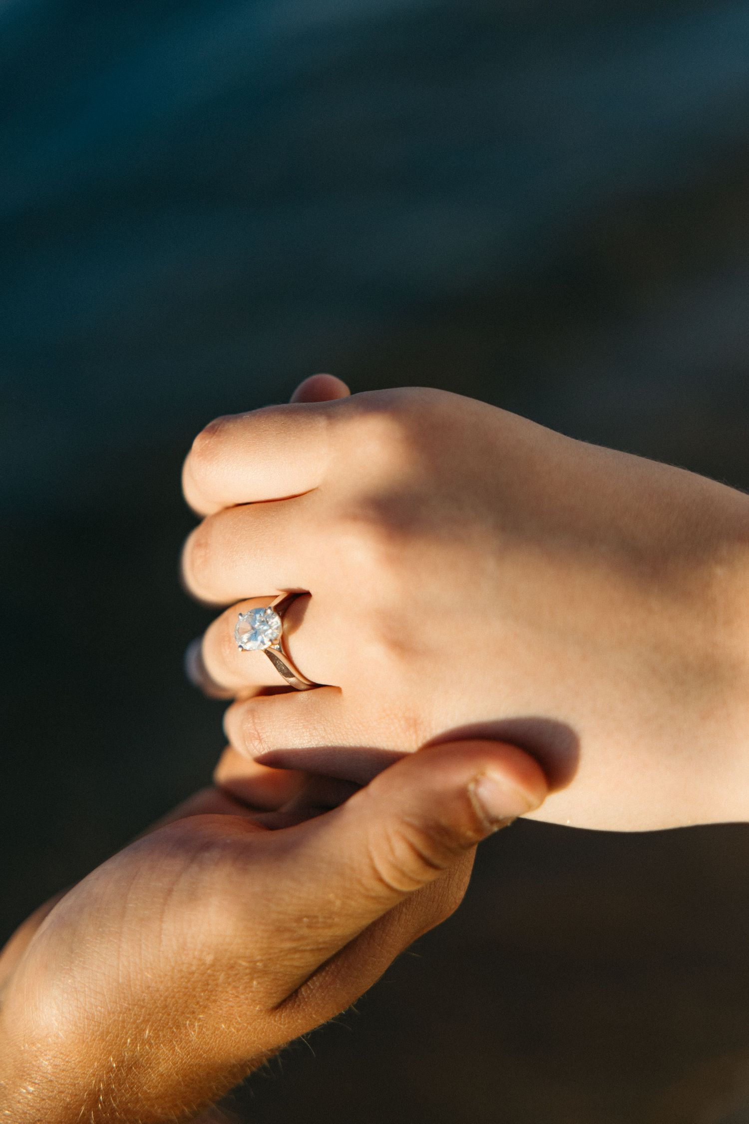 Close-up of engagement ring on womans hand held by partner outdoors.
