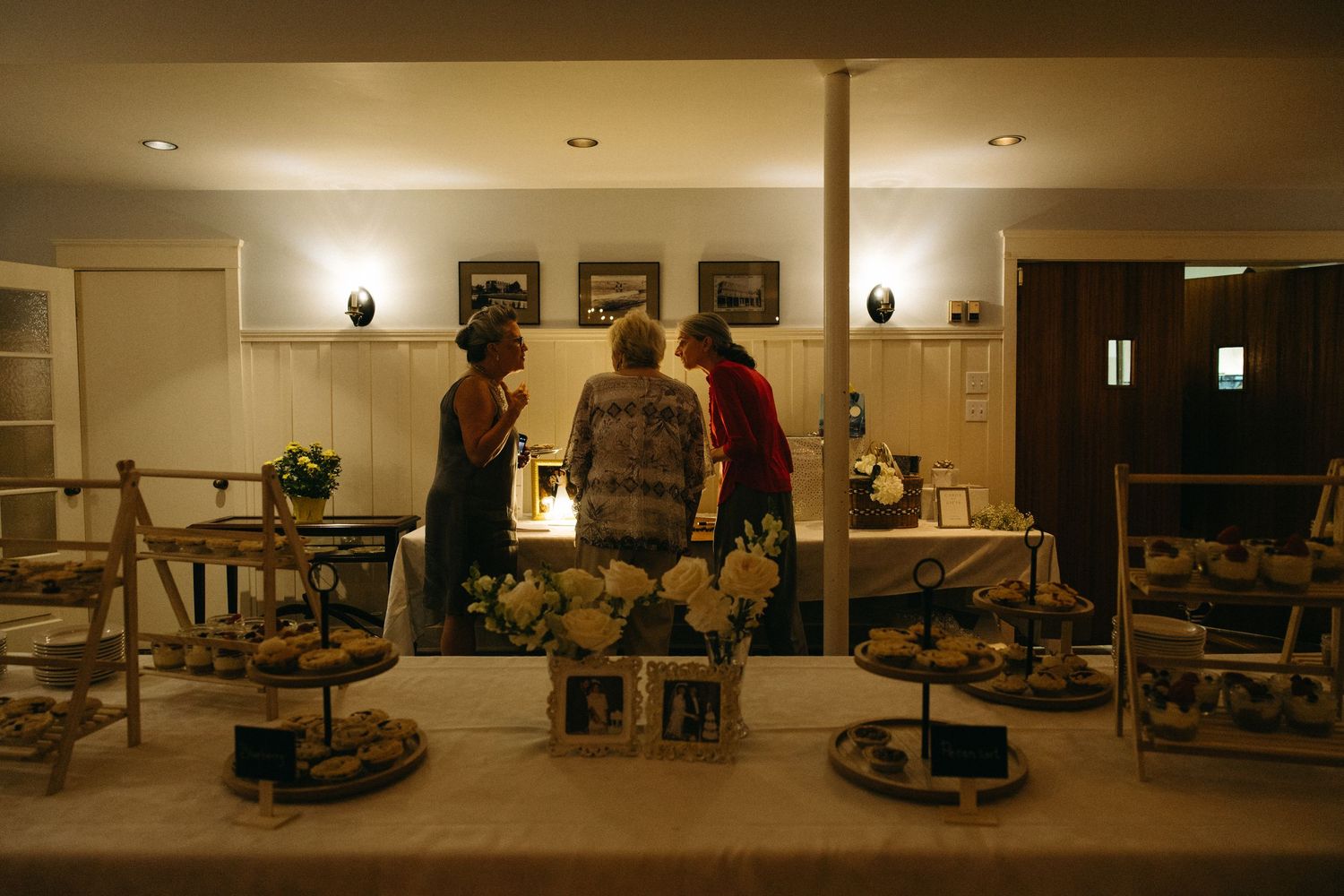 Wedding guests browse dessert table display in warmly lit reception venue during evening celebration.