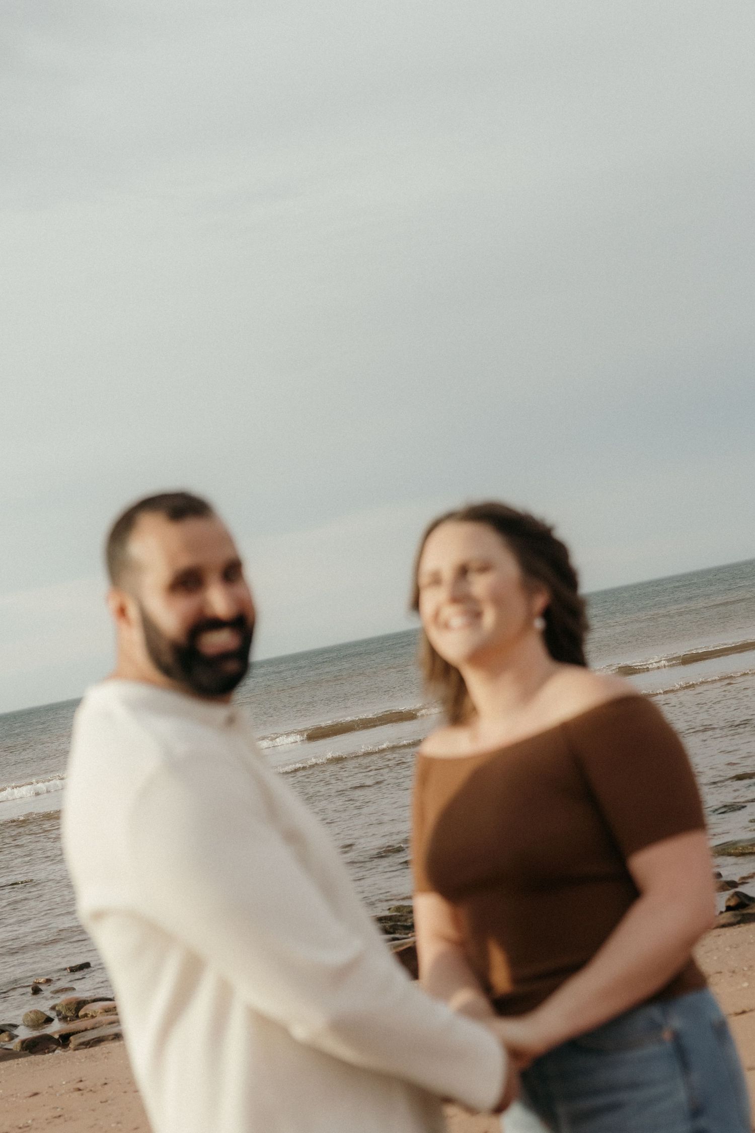 Two people sharing laughter and embracing on a sandy beach.