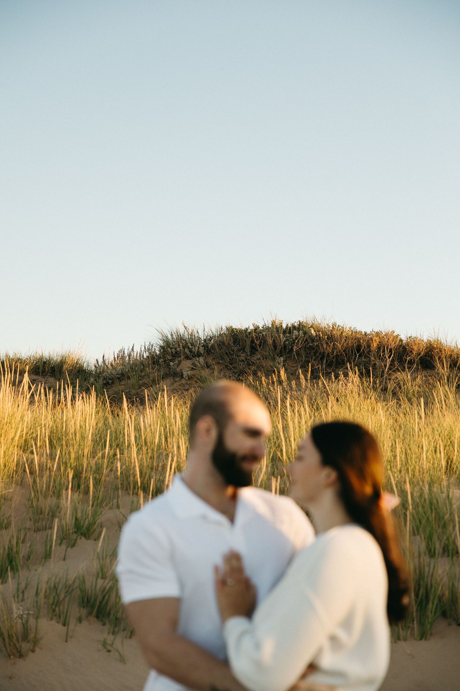 Intimate moments captured against golden beach grass at sunset.