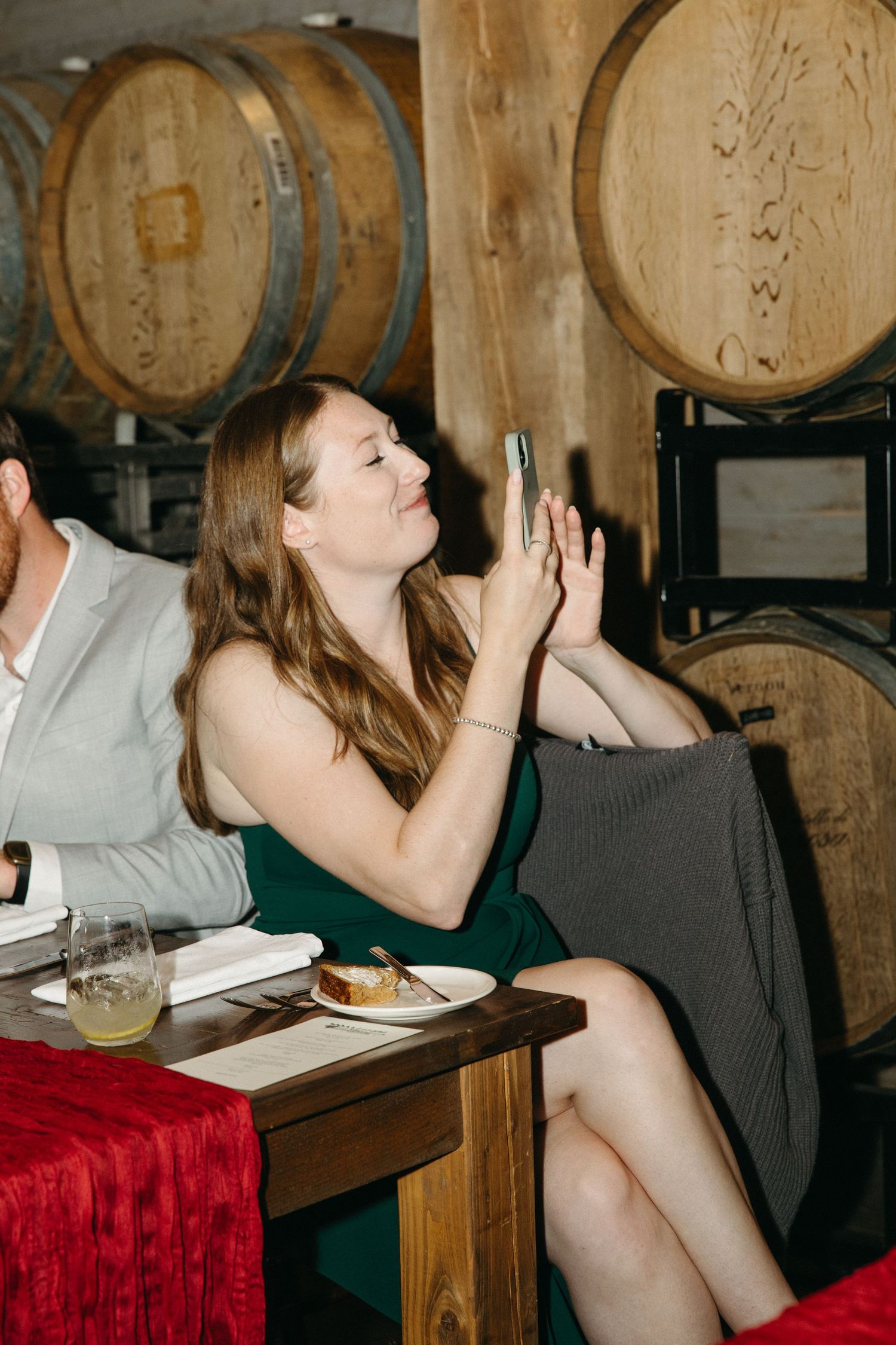 People celebrating at a rustic wine cellar dinner with wooden barrels in the background.