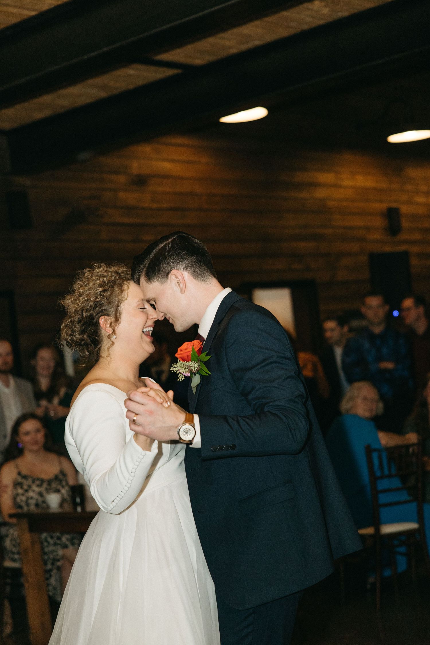 Romantic first dance moment in a rustic reception venue with wooden ceiling beams.