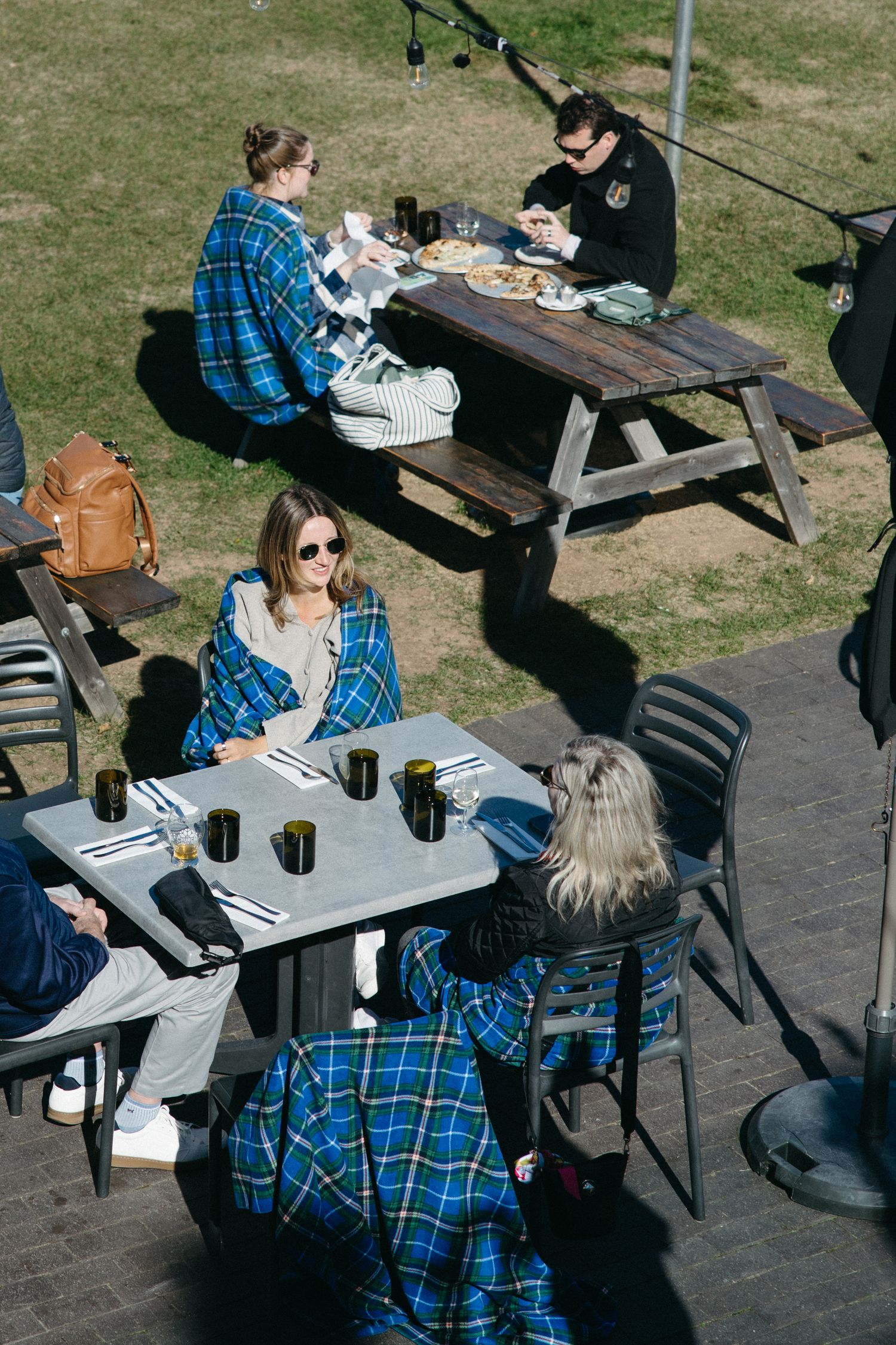 People enjoying outdoor dining at picnic tables on a sunny day.