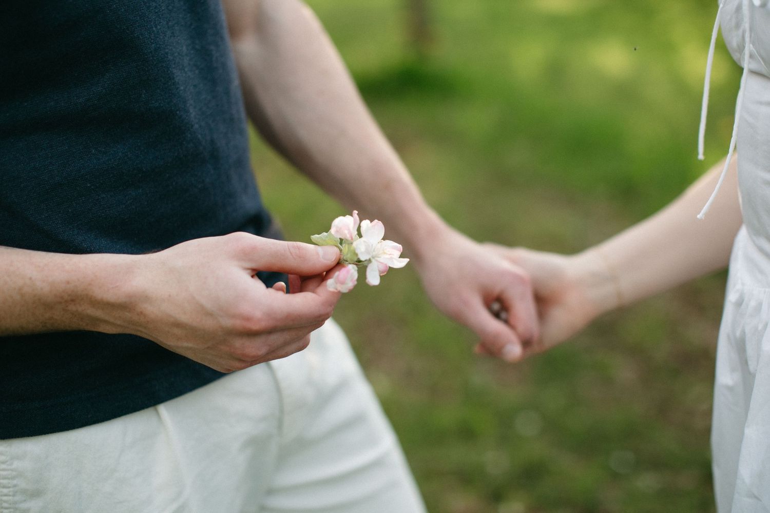Couple exchanging delicate pink cherry blossoms outdoors, symbolizing romance and connection in a lush green garden.