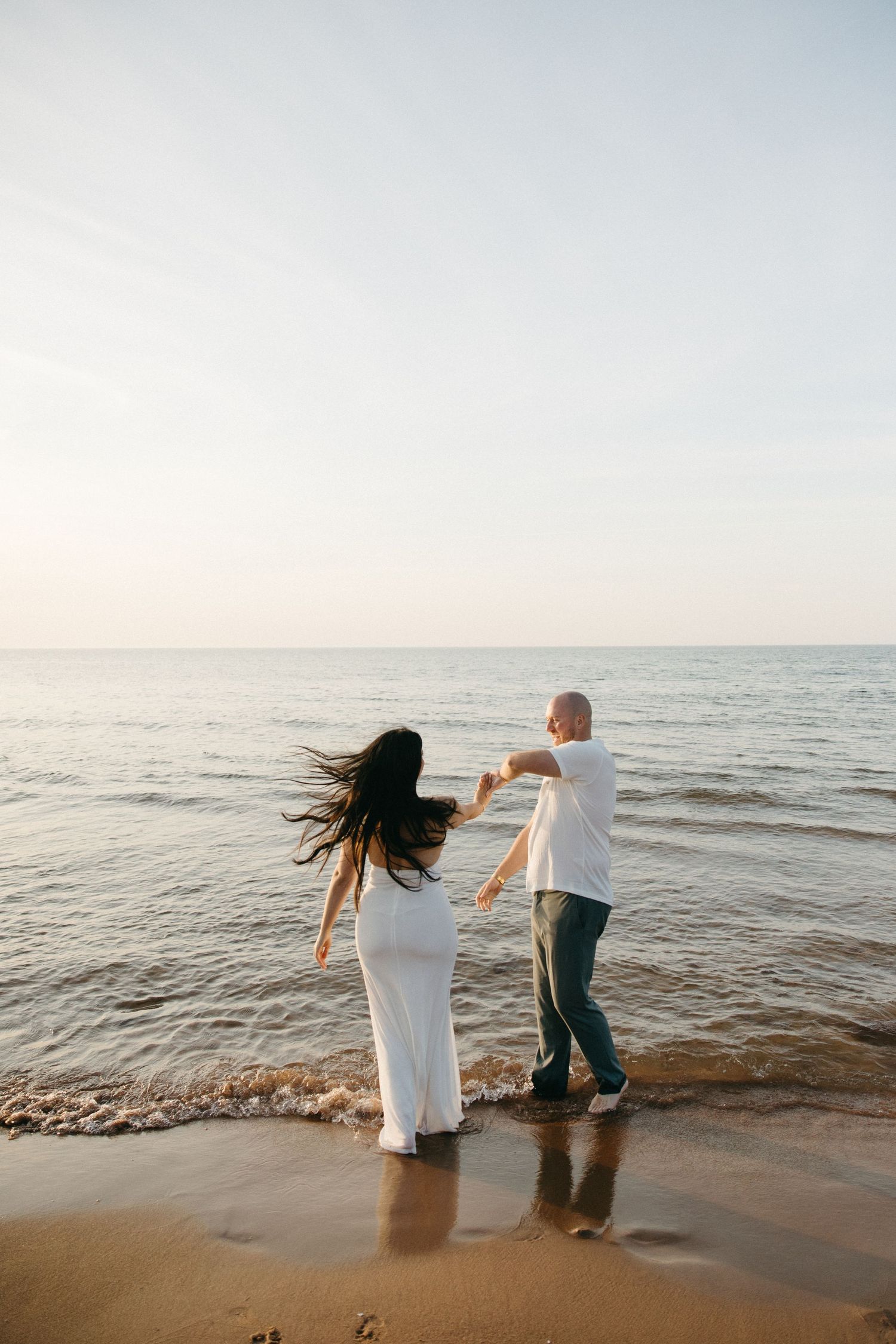 A couple dancing together on a sandy beach at sunset, with ocean waves gently washing ashore.