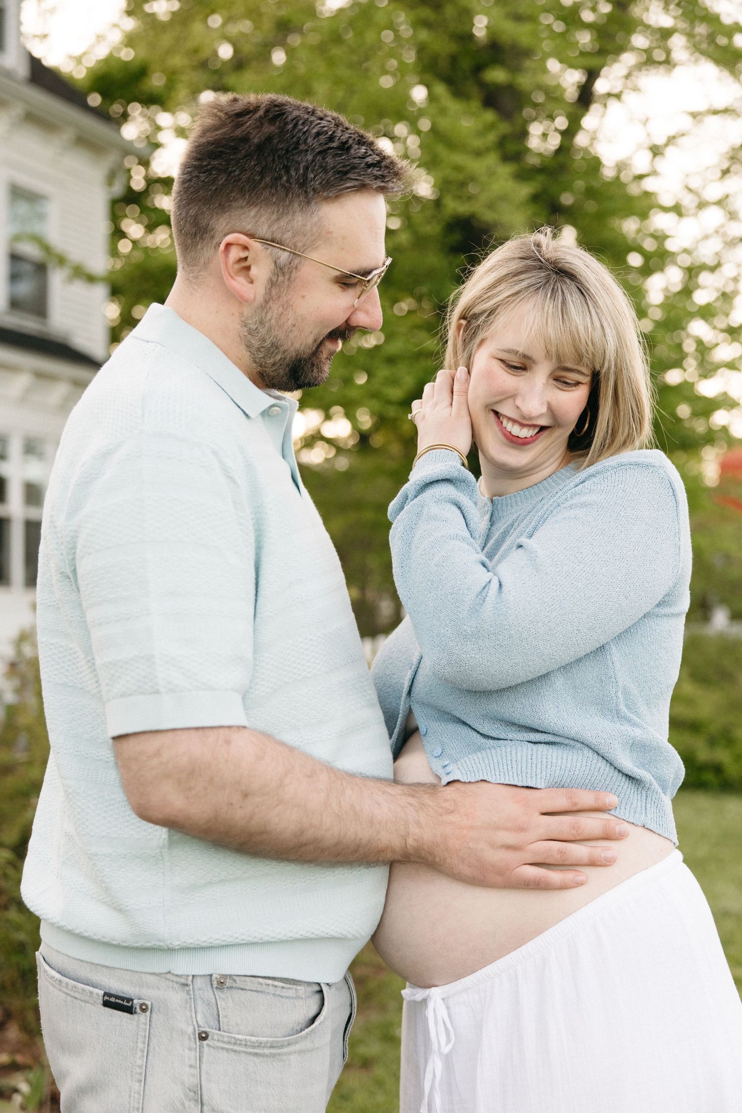 Smiling couple in matching light blue outfits share a joyful moment outdoors, with woman showing a pregnant belly.