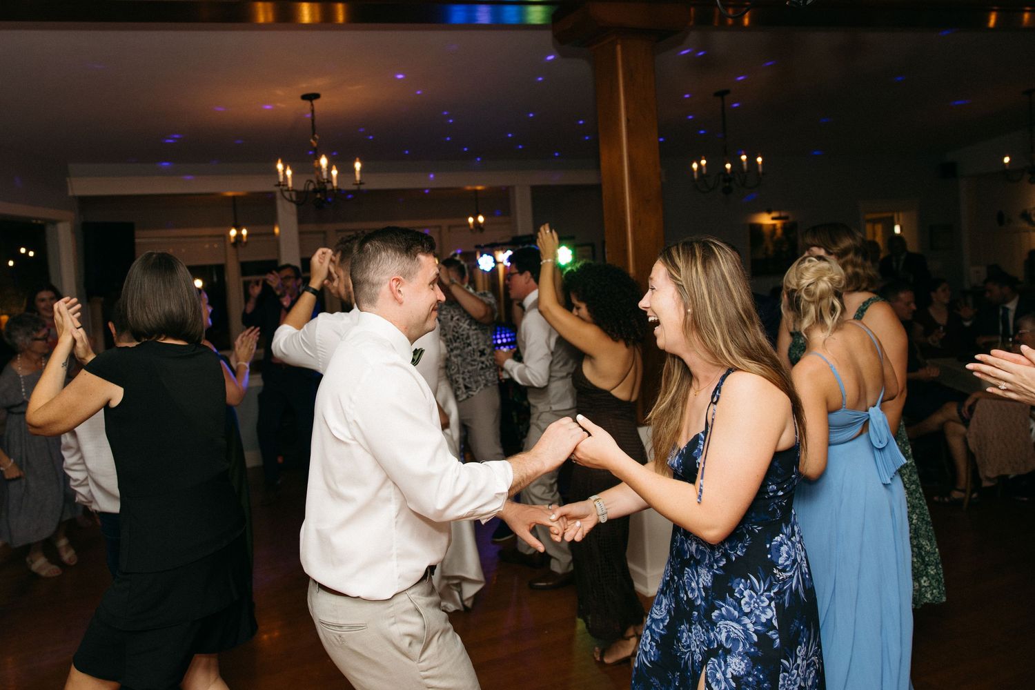 Guests dancing and celebrating joyfully on the dance floor at a lively wedding reception.
