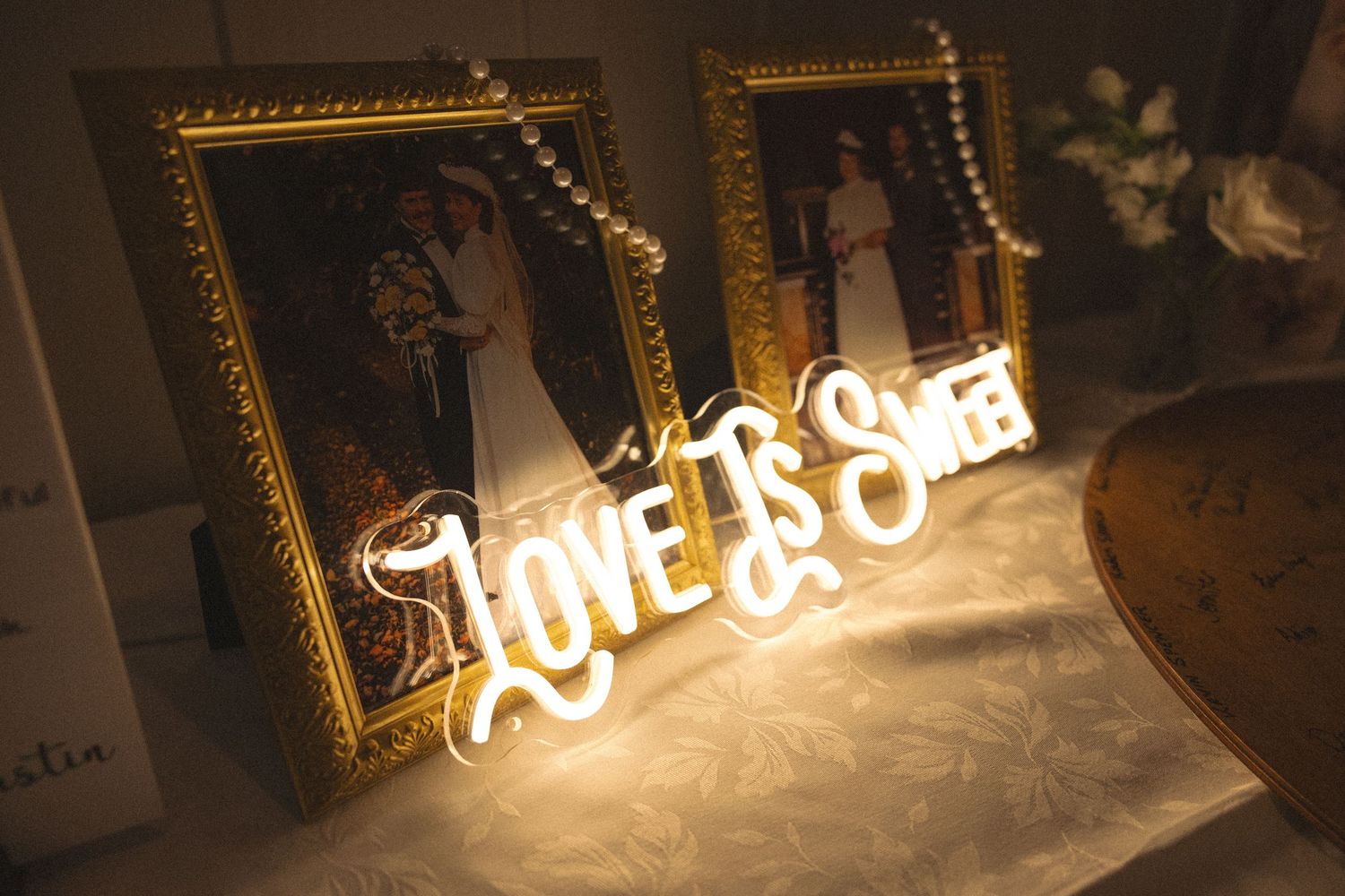 Glowing neon Love Is Sweet sign displayed between two framed wedding photos at a reception.