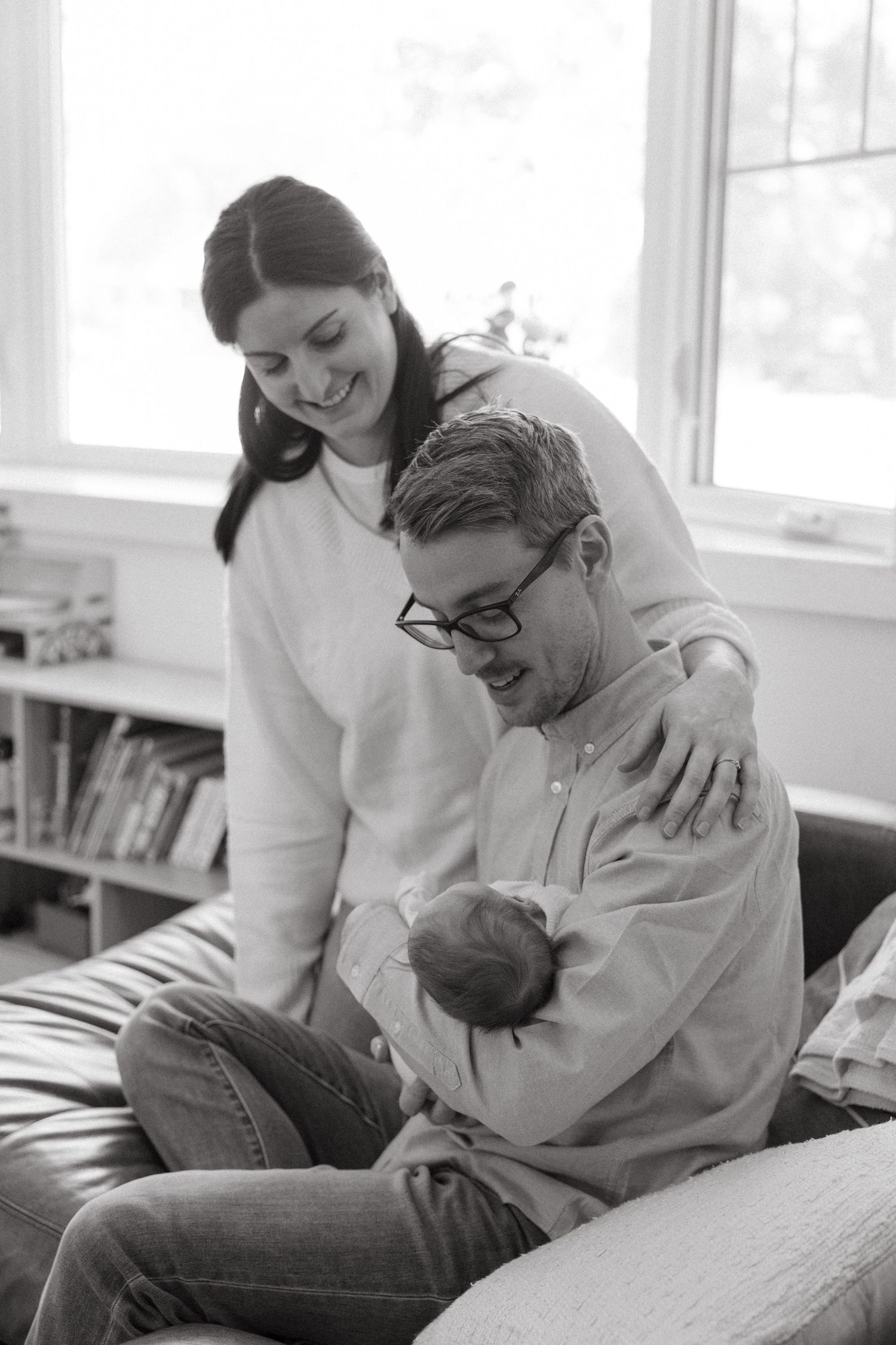Candid black and white photos capturing intimate family moments on couch by window.