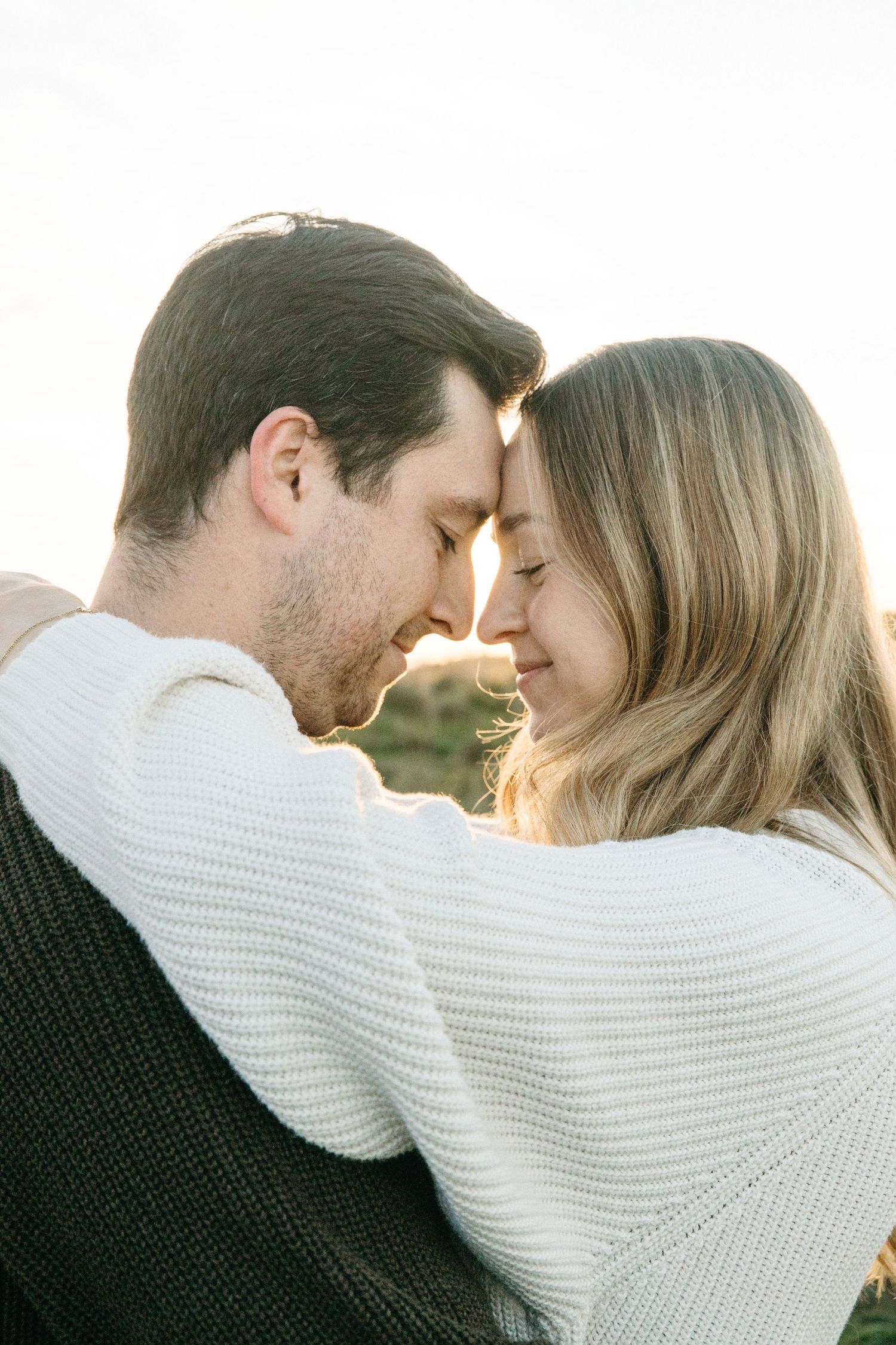 Couple touching foreheads with eyes closed in a tender embrace during a warm golden hour engagement photo session.