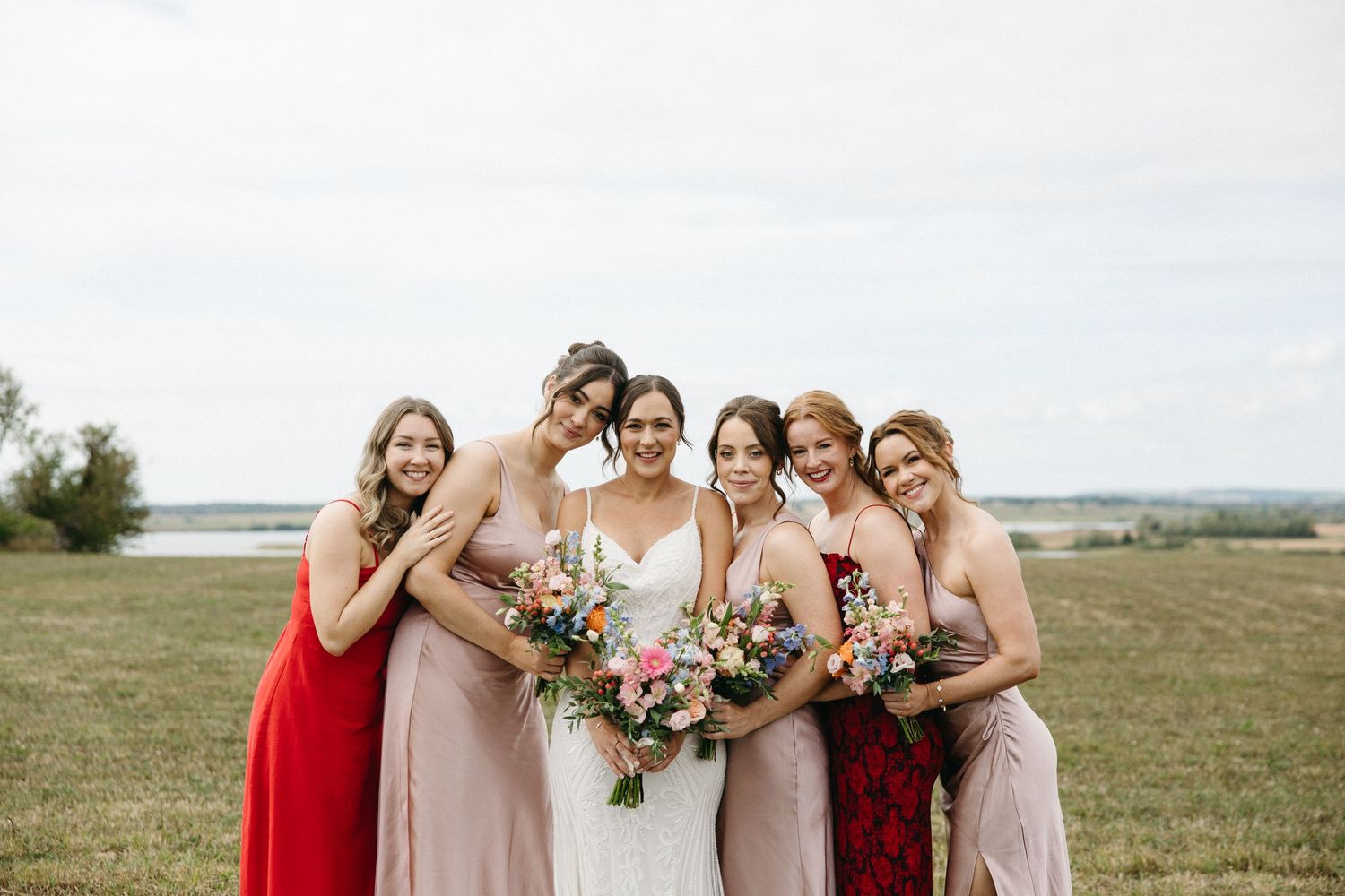 Bridal party in red and blush dresses poses together outdoors.