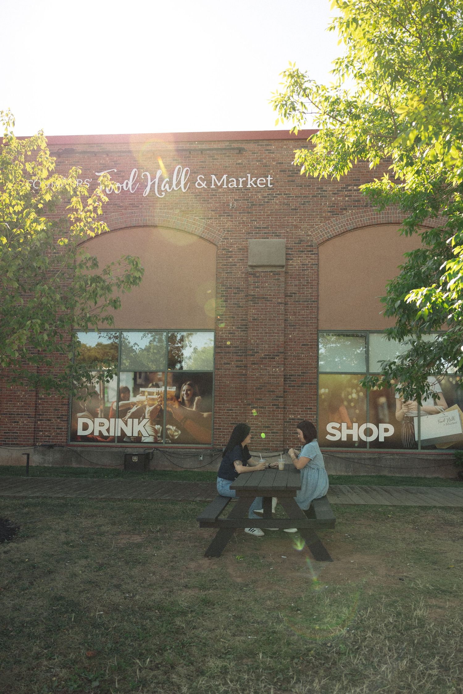 People enjoying a sunny day outside a brick building with 'Market' signage visible.