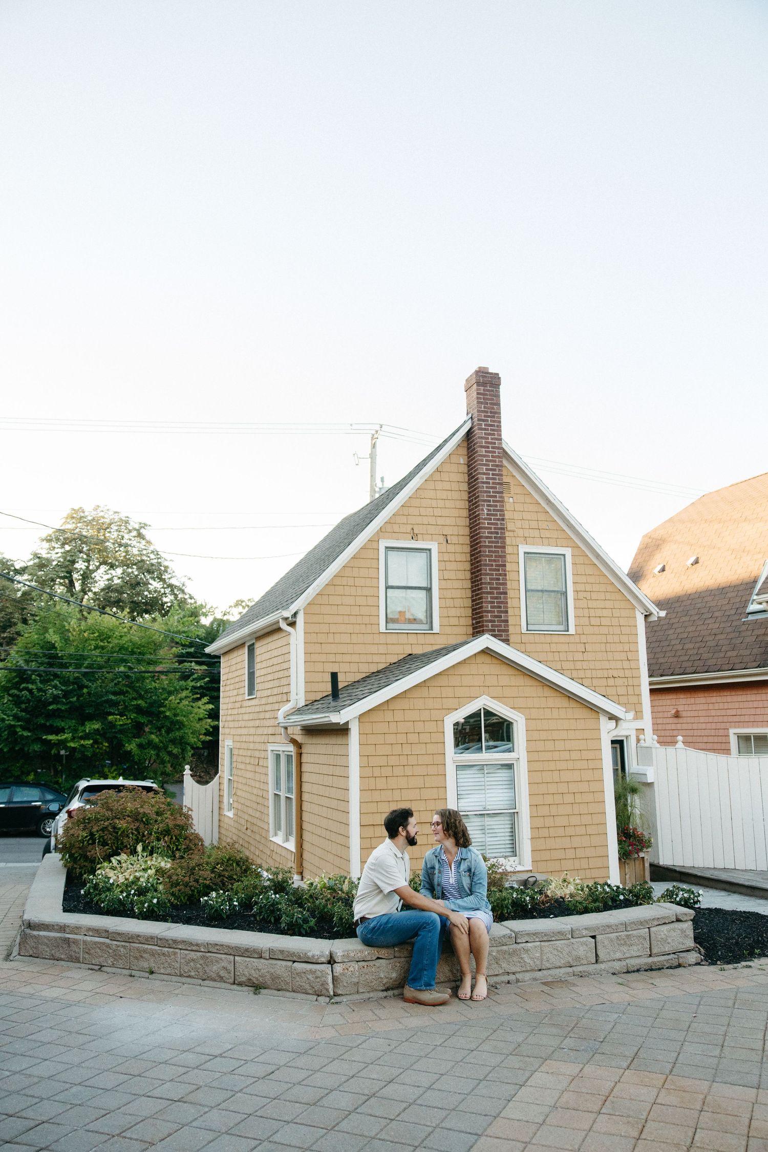 Two people share a moment outside traditional beige shingled houses at dusk.