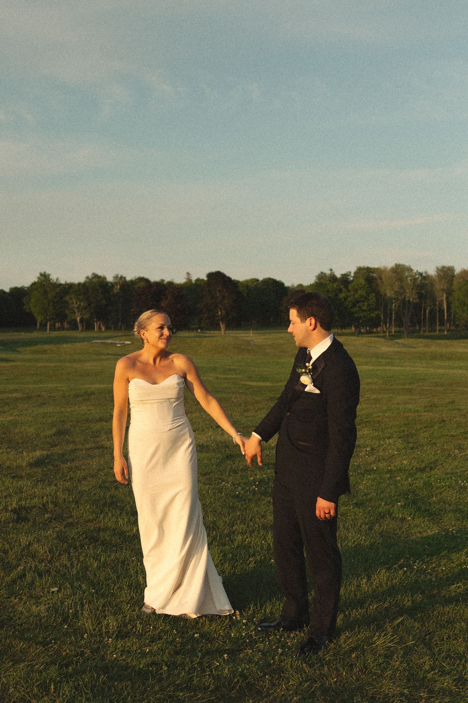 Newlyweds hold hands while walking on a golf course at golden hour.